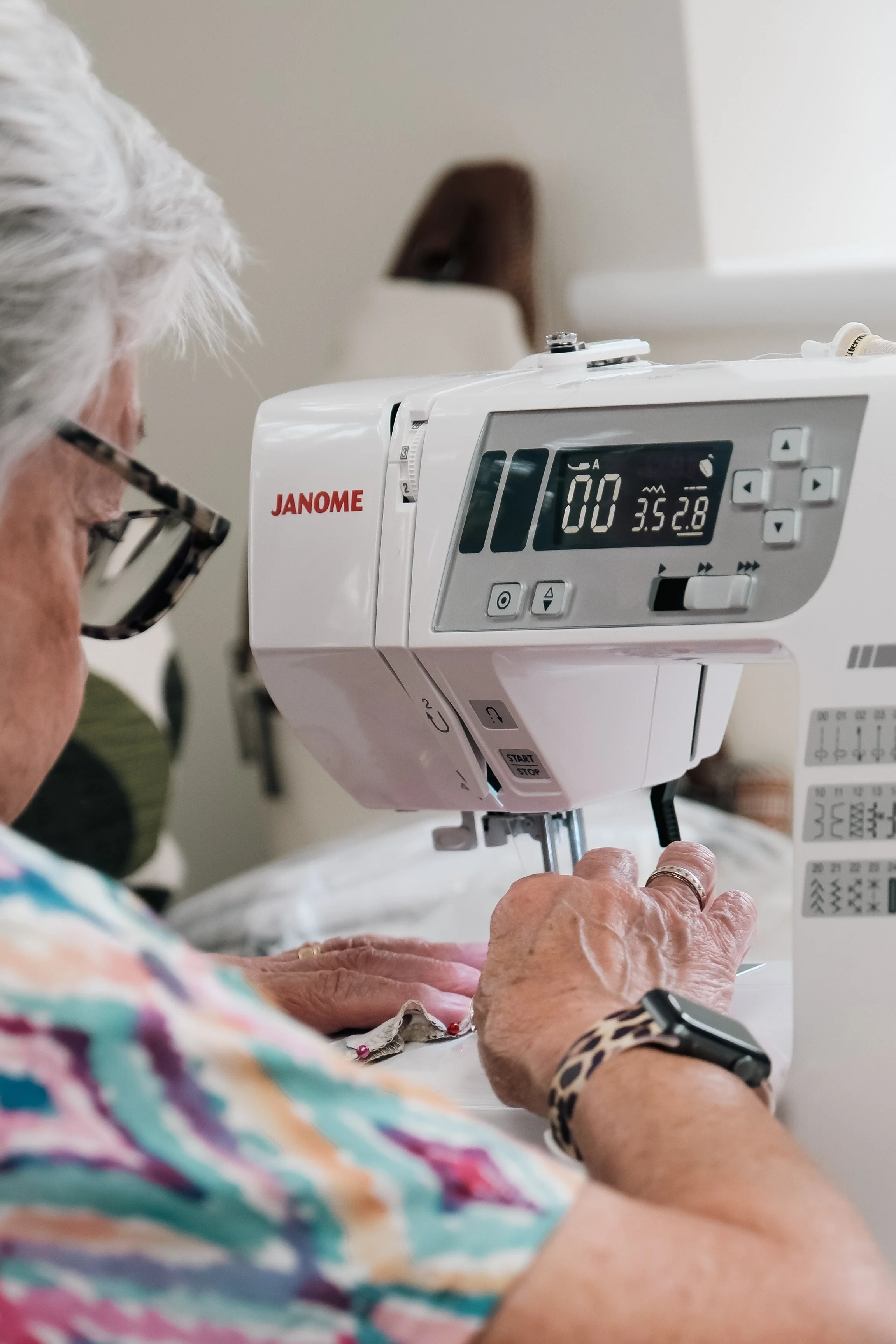An elderly person sewing with a sewing machine, focusing on their hands and the machine.