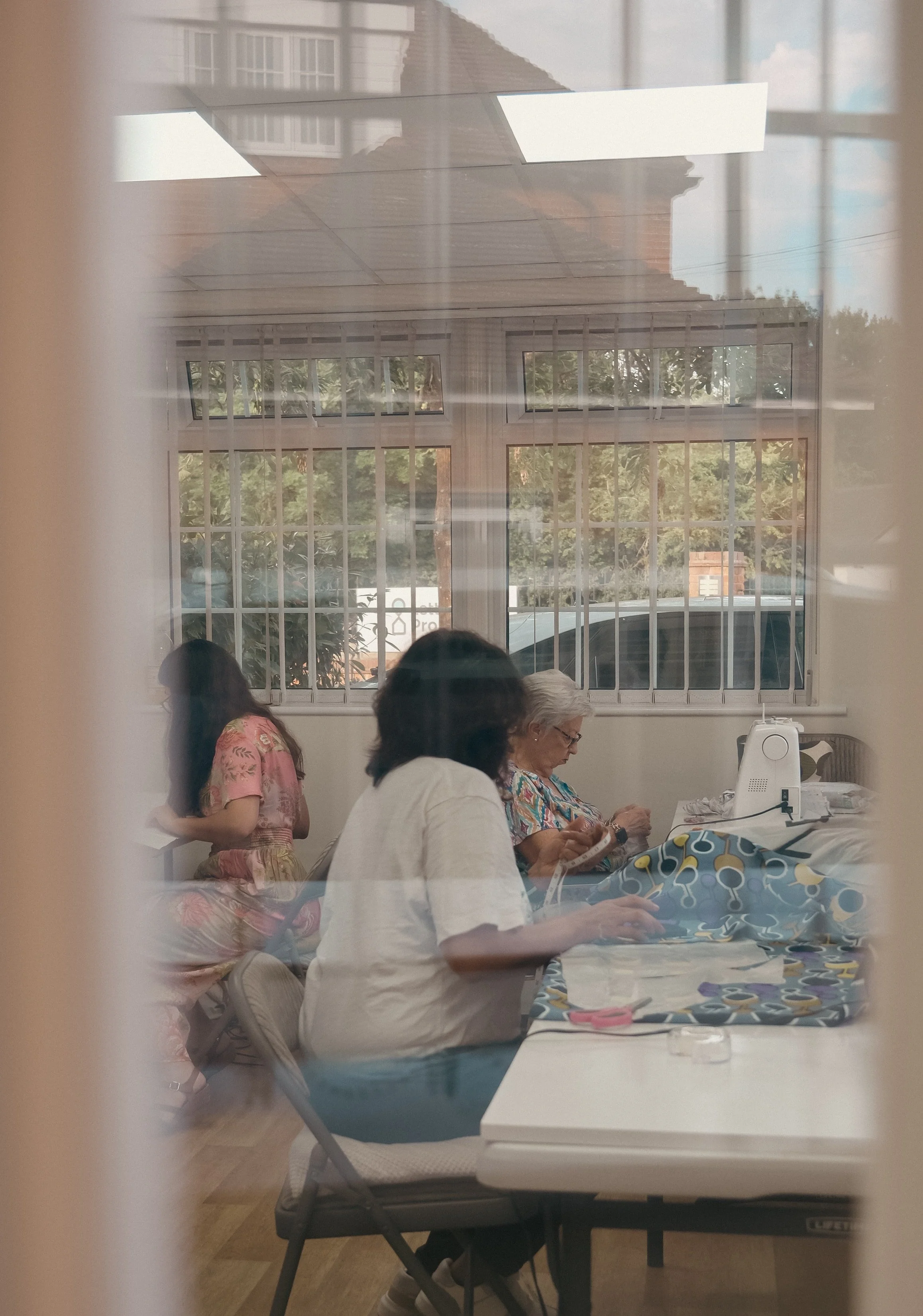 People sitting at a table inside a room with a large window, viewed through a glass window or door.