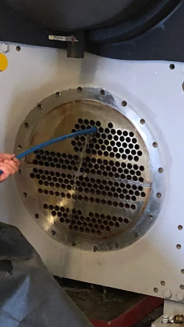 A person holding a blue hose near a large industrial heat exchanger or boiler with a circular metal opening