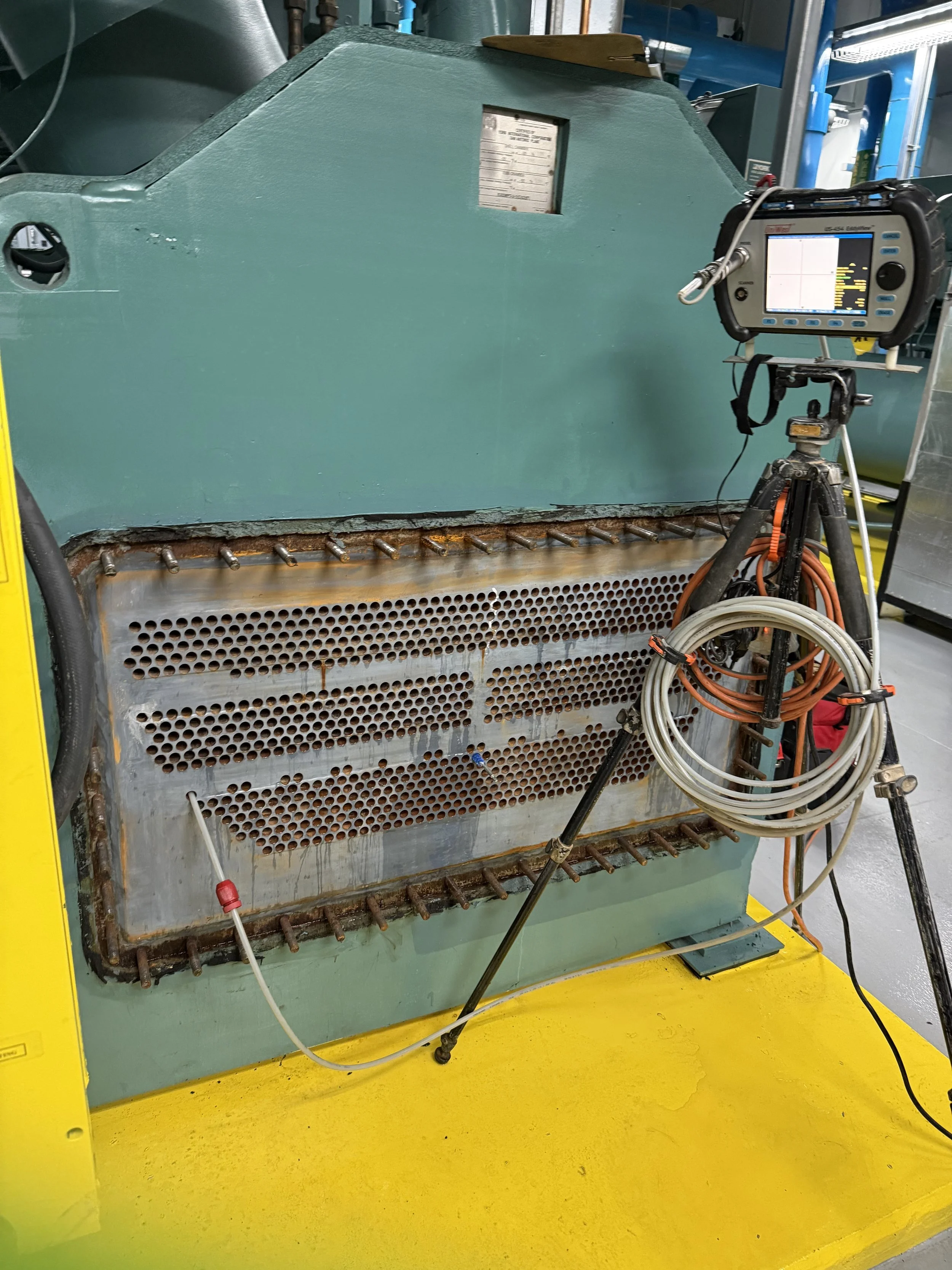 Industrial machine with a green metal enclosure, rusted lower section, and a digital display device mounted on a tripod with cables