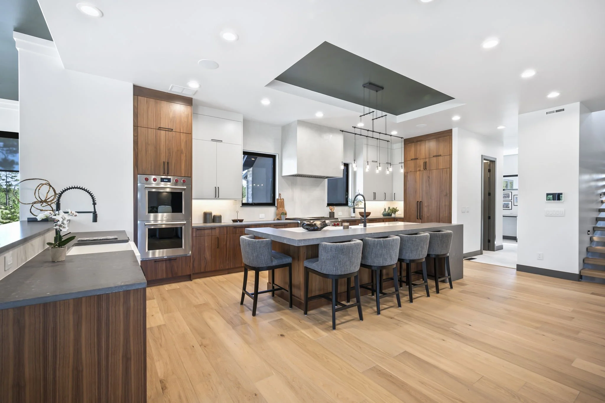 Modern kitchen with white and wooden cabinetry, island with gray countertop, bar stools, and pendant lighting.