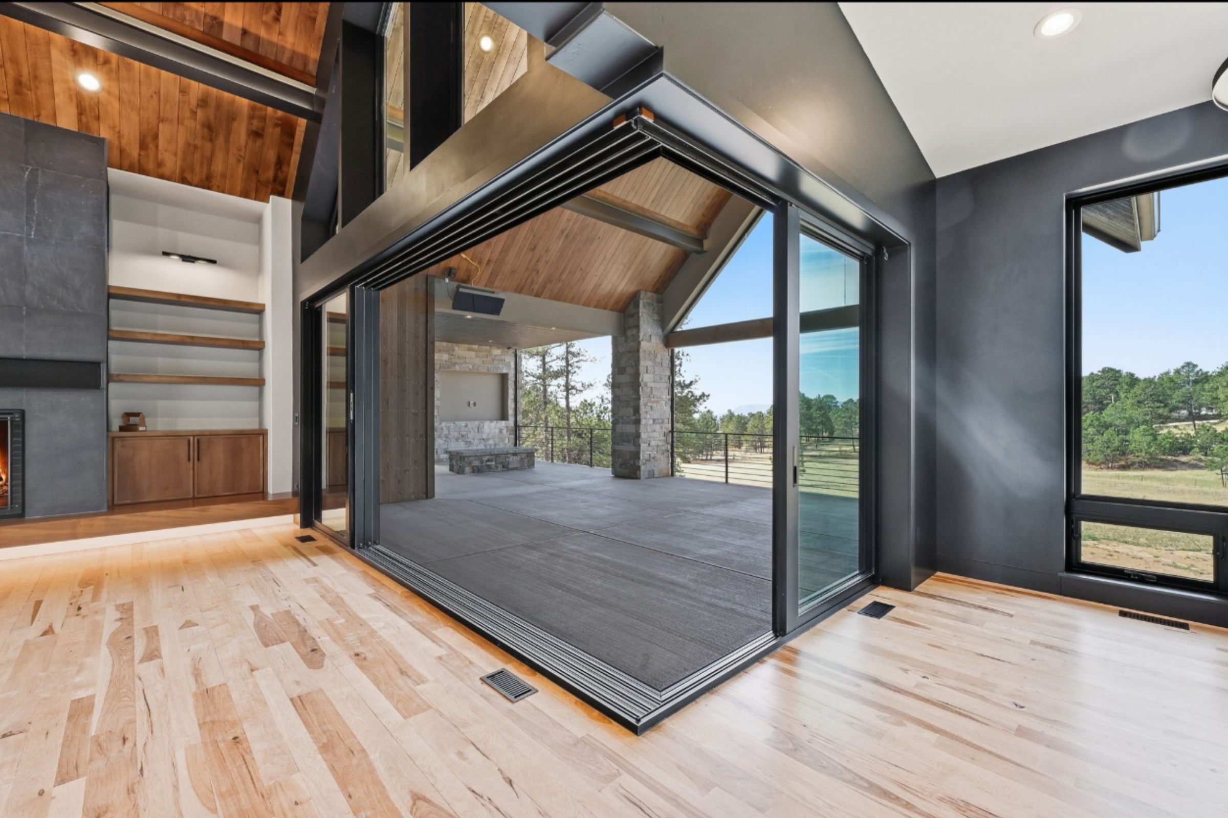 Modern living room with large glass sliding doors opening to an outdoor patio, featuring a mix of wood and stone interior design elements.