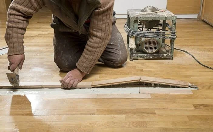 Person installing wood flooring with a saw on a portable table, kneeling on the floor in a workspace.