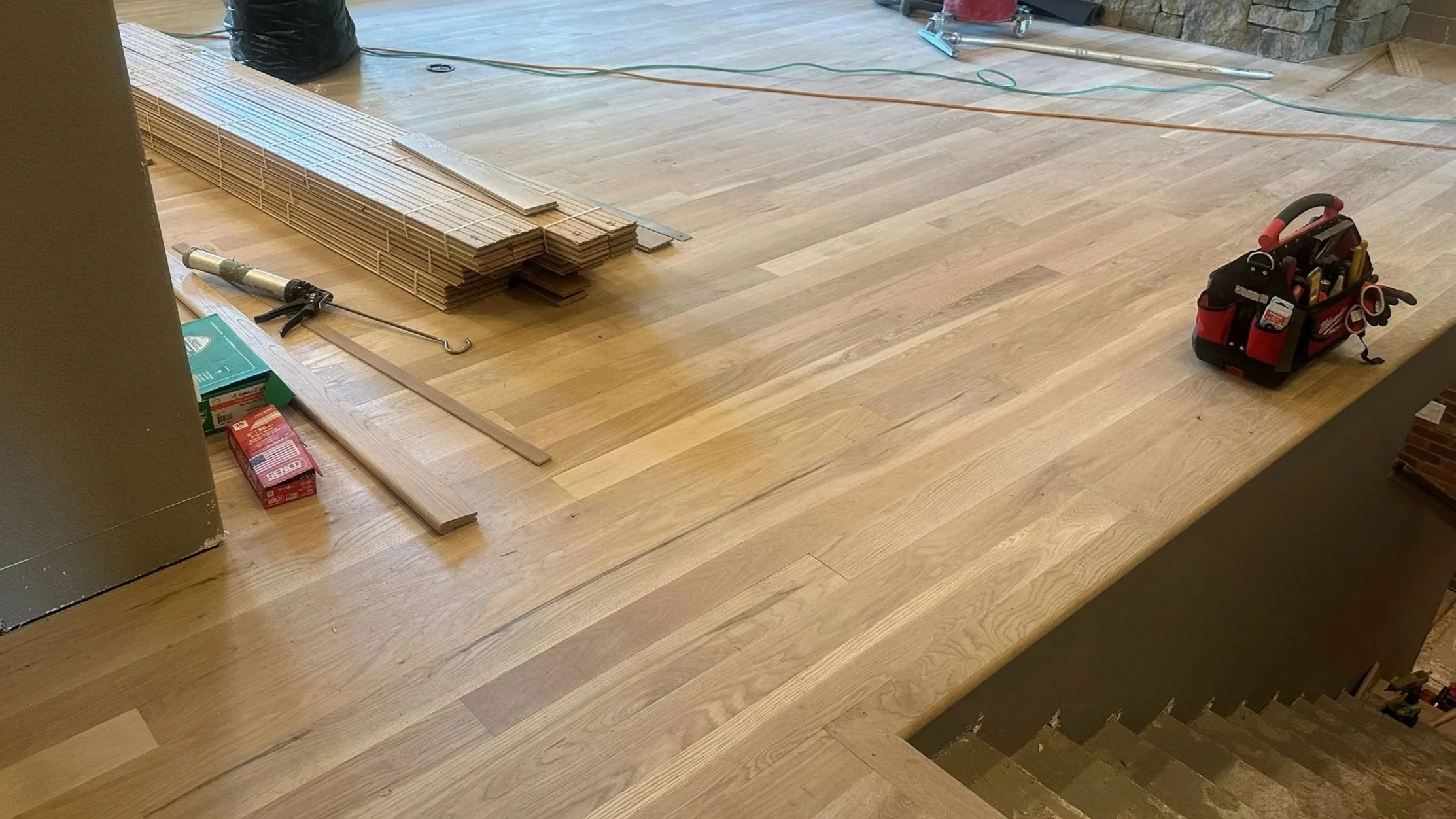 Wood flooring installation in progress with tools and supplies on a partially finished hardwood floor.