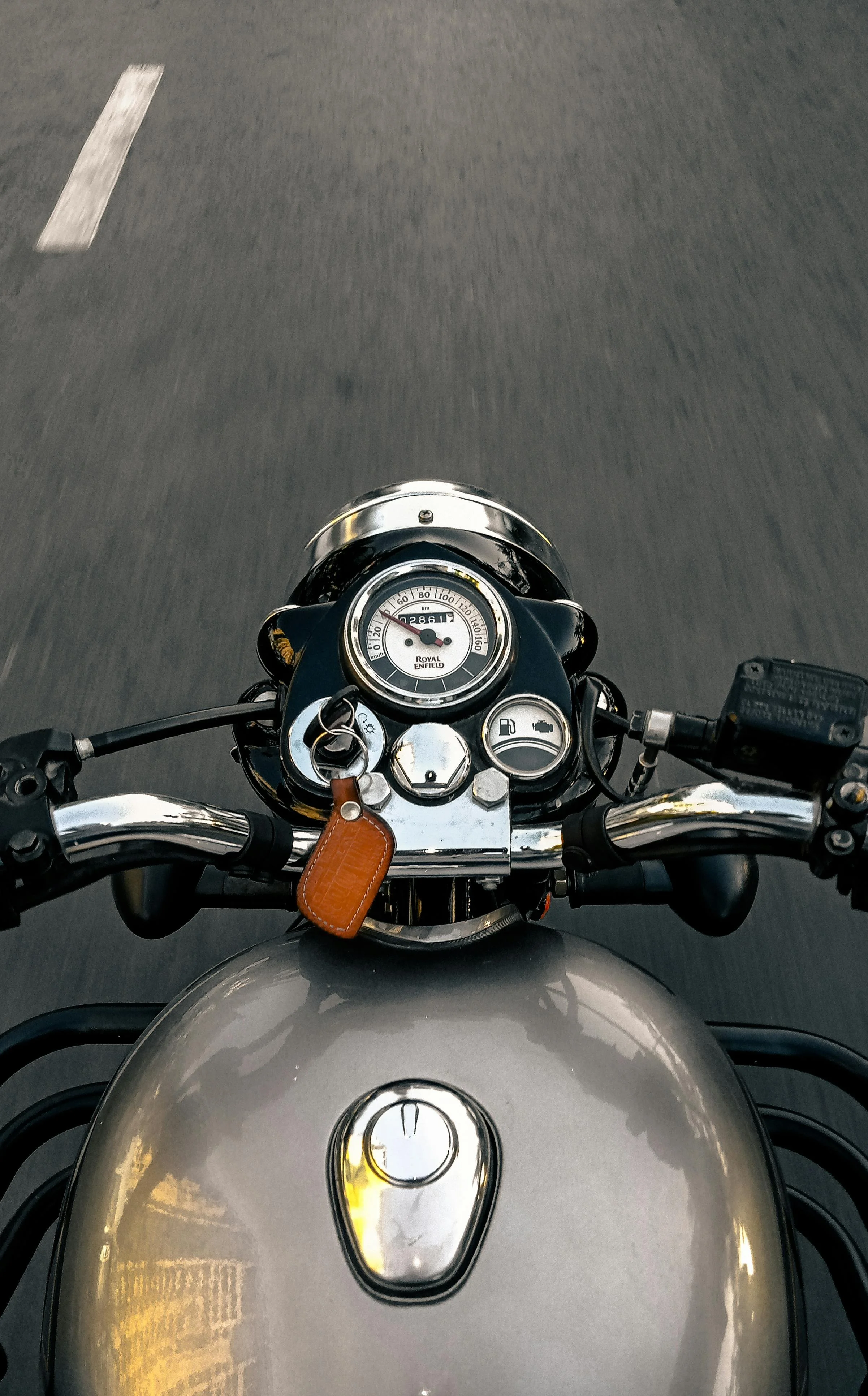 Overhead view of a motorcycle's dashboard and handlebars, showing the speedometer, fuel gauge, and dashboard lights, with part of the motorcycle's fuel tank in the foreground.