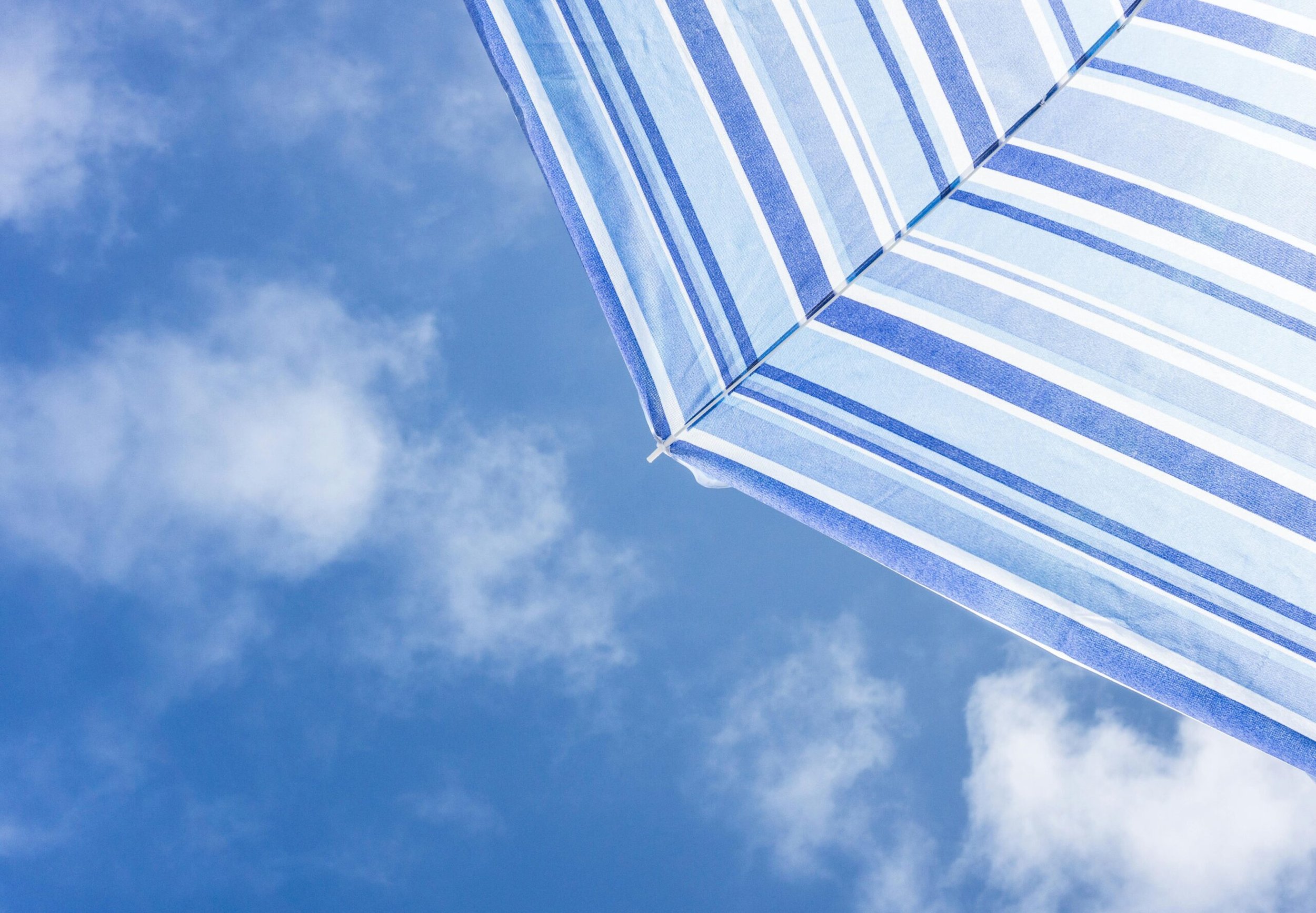 Blue and white striped beach umbrella against a cloudy blue sky.