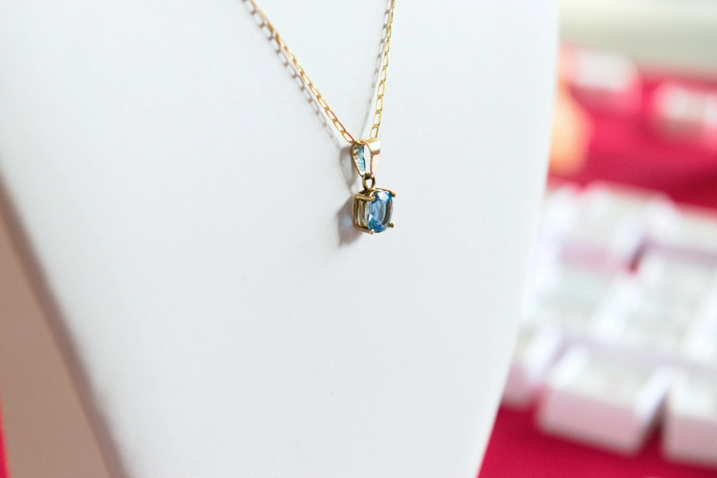 A gold necklace with a rectangular blue gemstone pendant hanging on a white display bust.