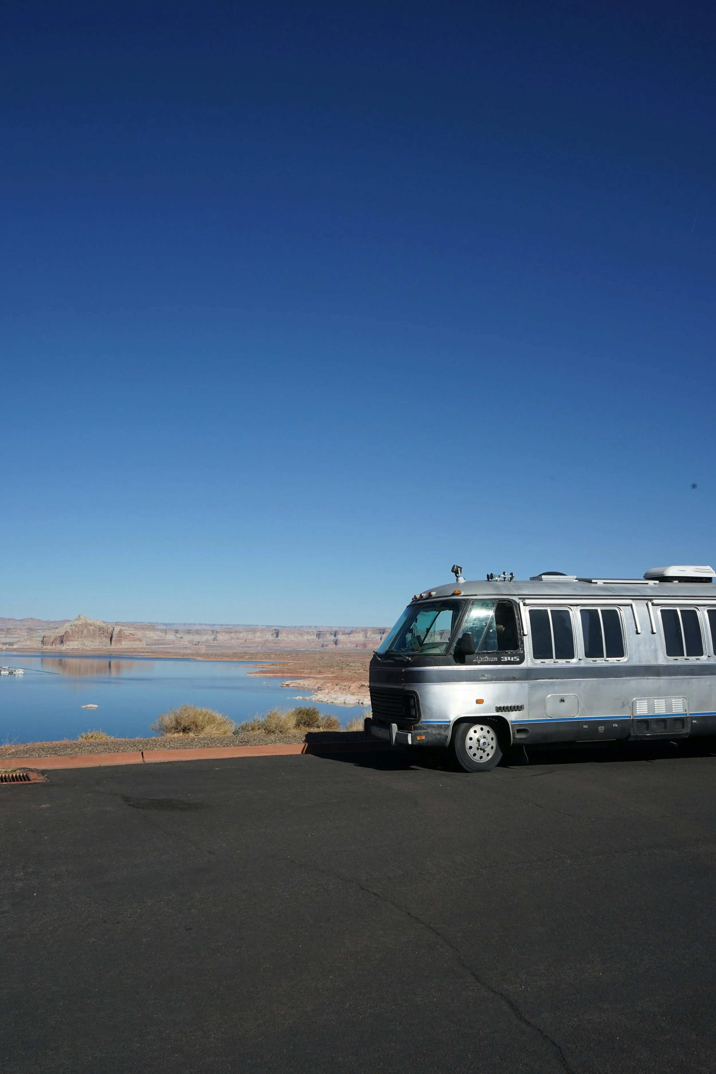 A silver vintage camper van parked on a paved area overlooking a body of water with which is written with Hardin insurance's coverage.