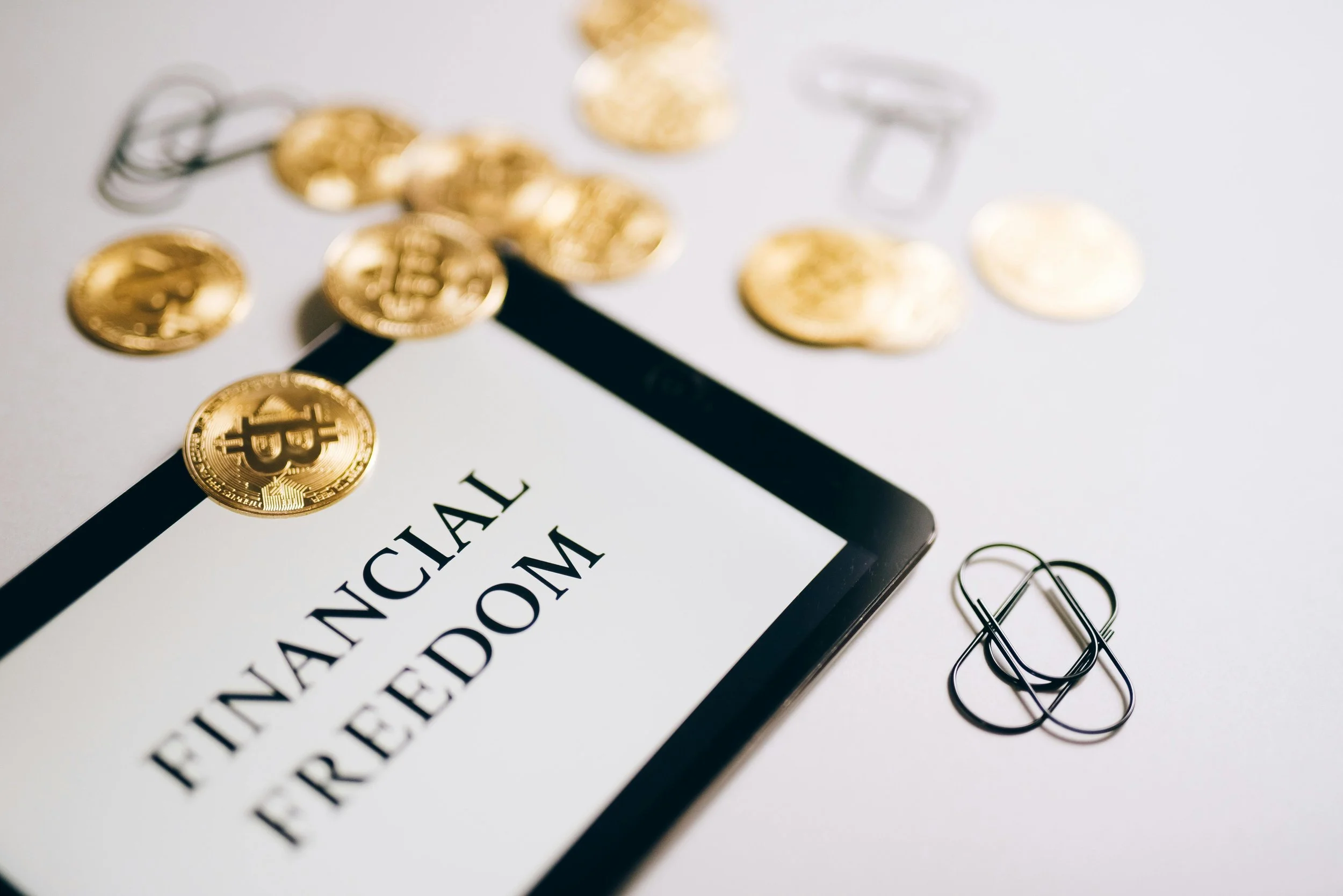 Close-up of a document with gold Bitcoin coins, paper clips, and binder clips placed on and around it, with part of a printed document visible.