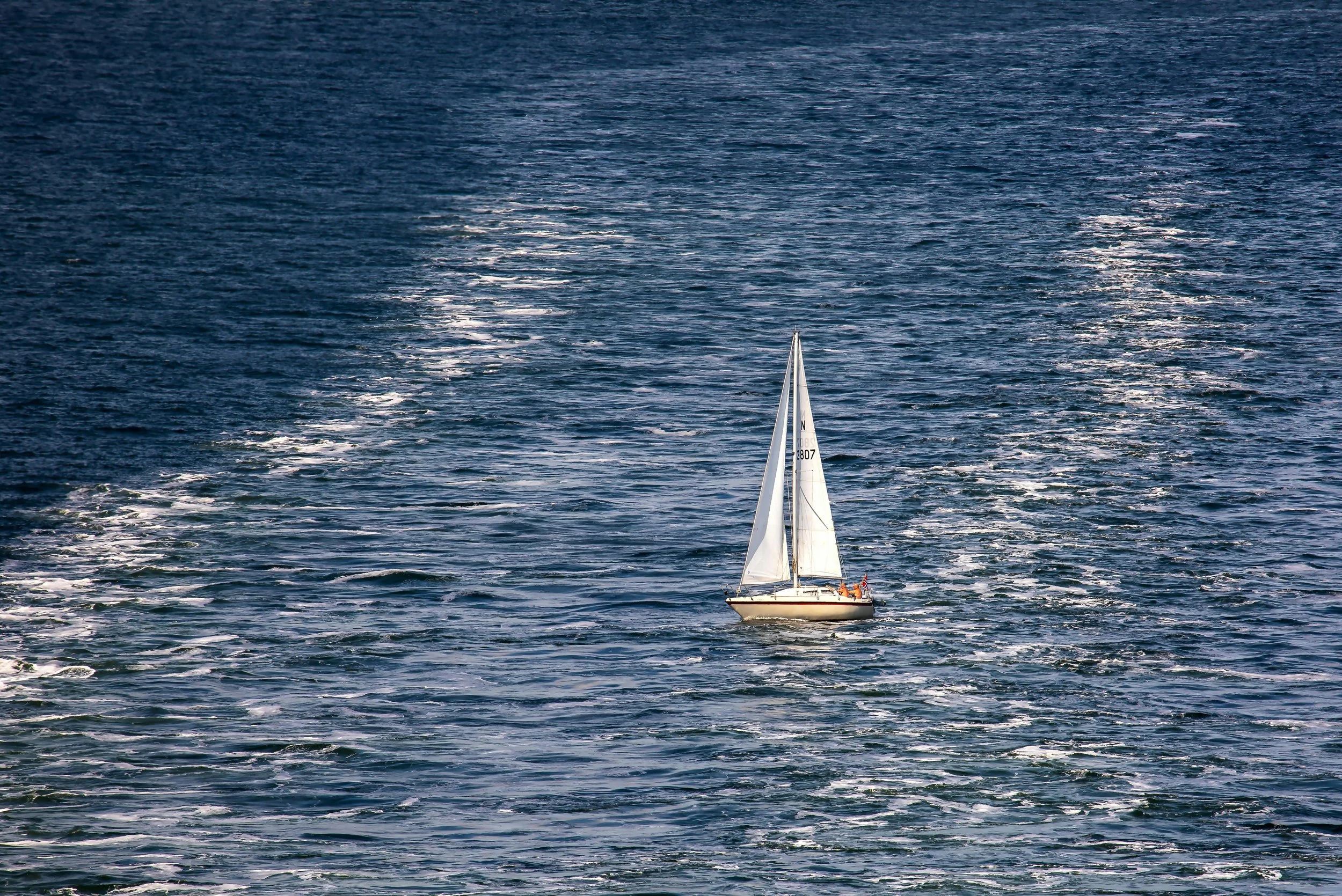 A sailboat navigating on the open ocean with a trail of white waves behind it.