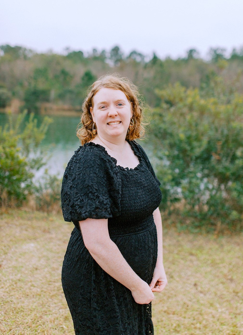 Christina Walker, a consulting agent with Hardin insurance wearing a black lace dress, standing outdoors with a lake and trees in the background at her Callahan Home.