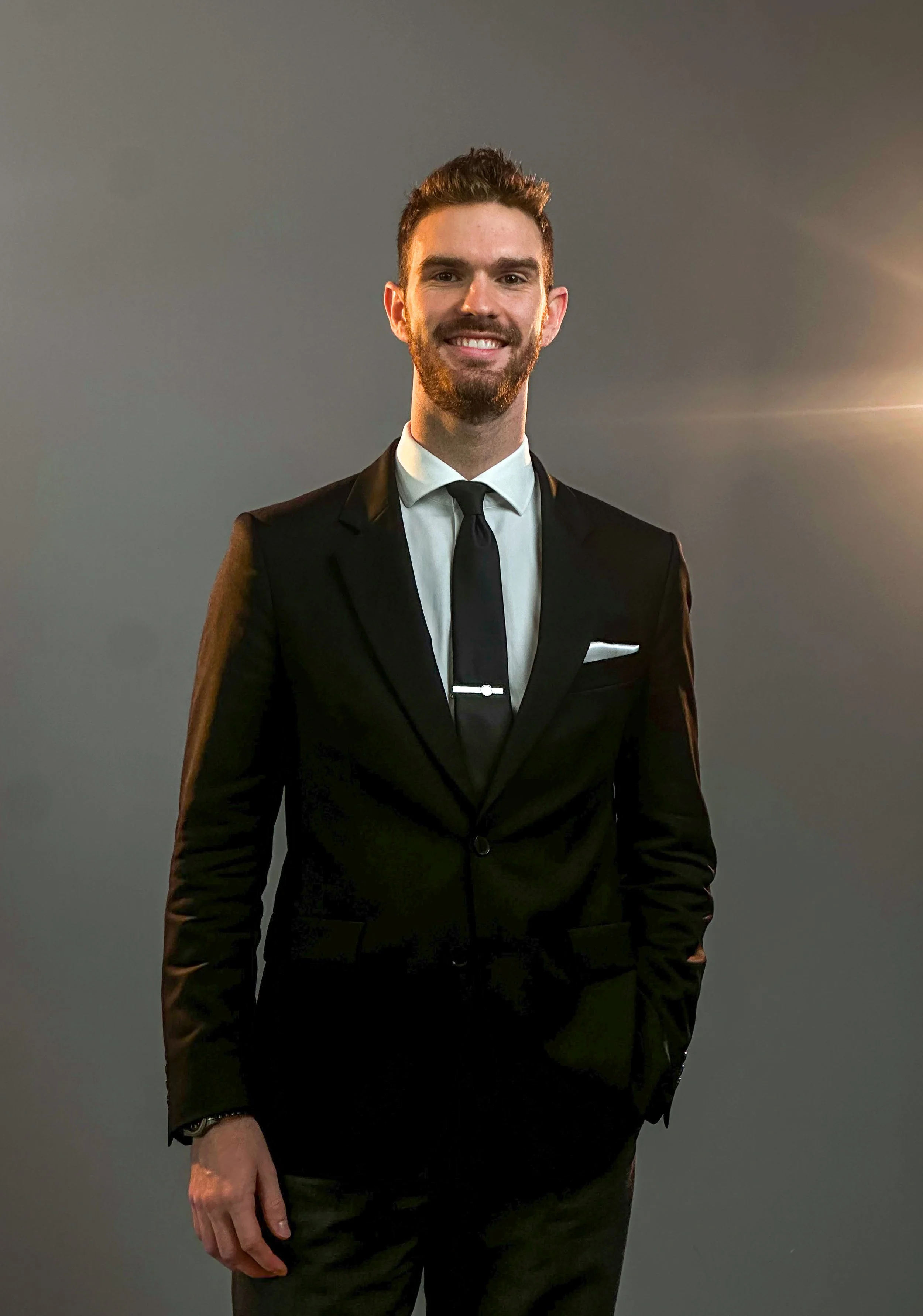 Stephen Hardin customer service representative for Hardin Insurance  dressed in a black suit, white shirt, and black tie, smiling against a dark background.
