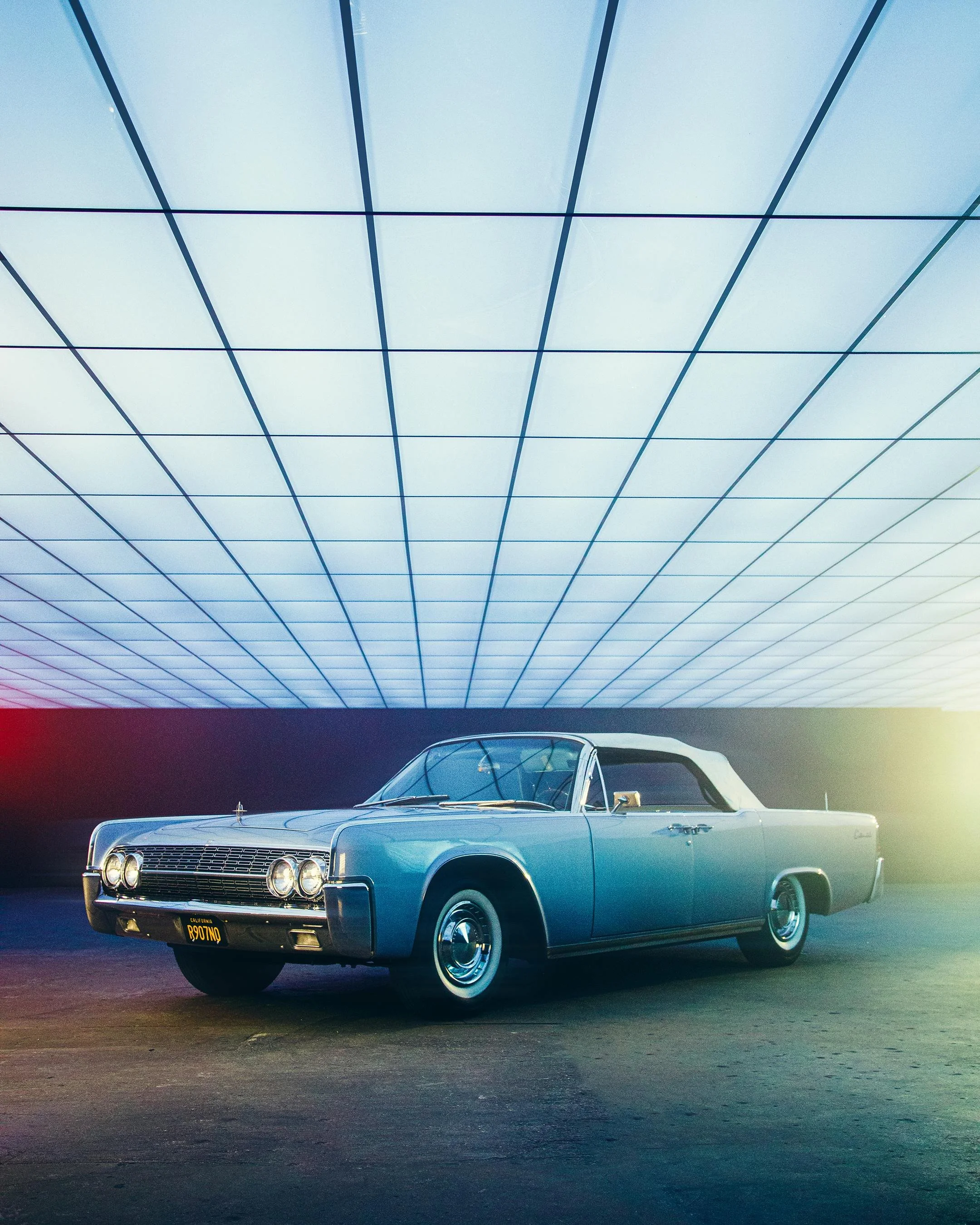 A classic light blue vintage car with chrome accents parked in front of a modern glass building with a grid pattern.