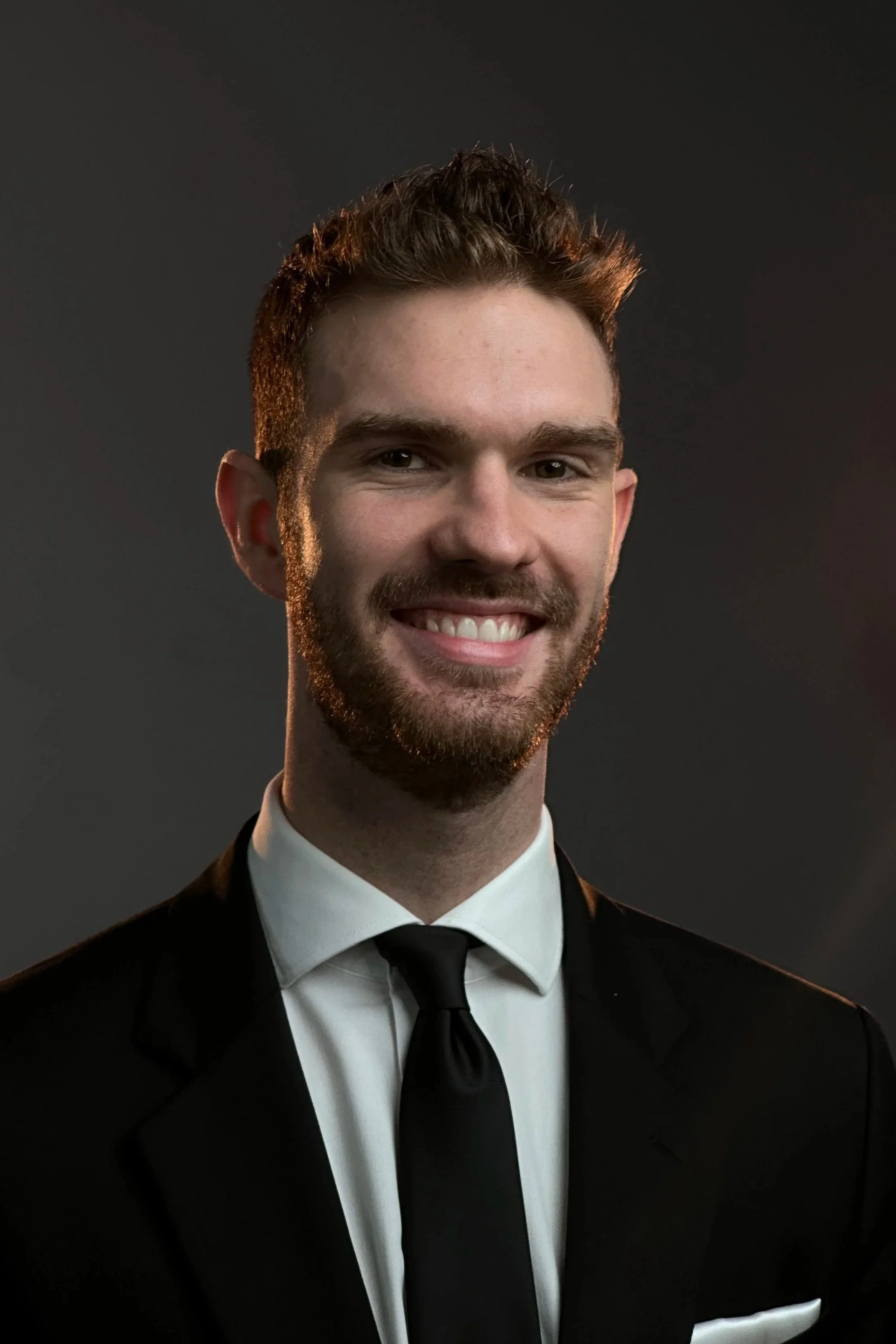 Stephen Hardin customer service representative for Hardin Insurance  dressed in a black suit, white shirt, and black tie, smiling against a dark background.