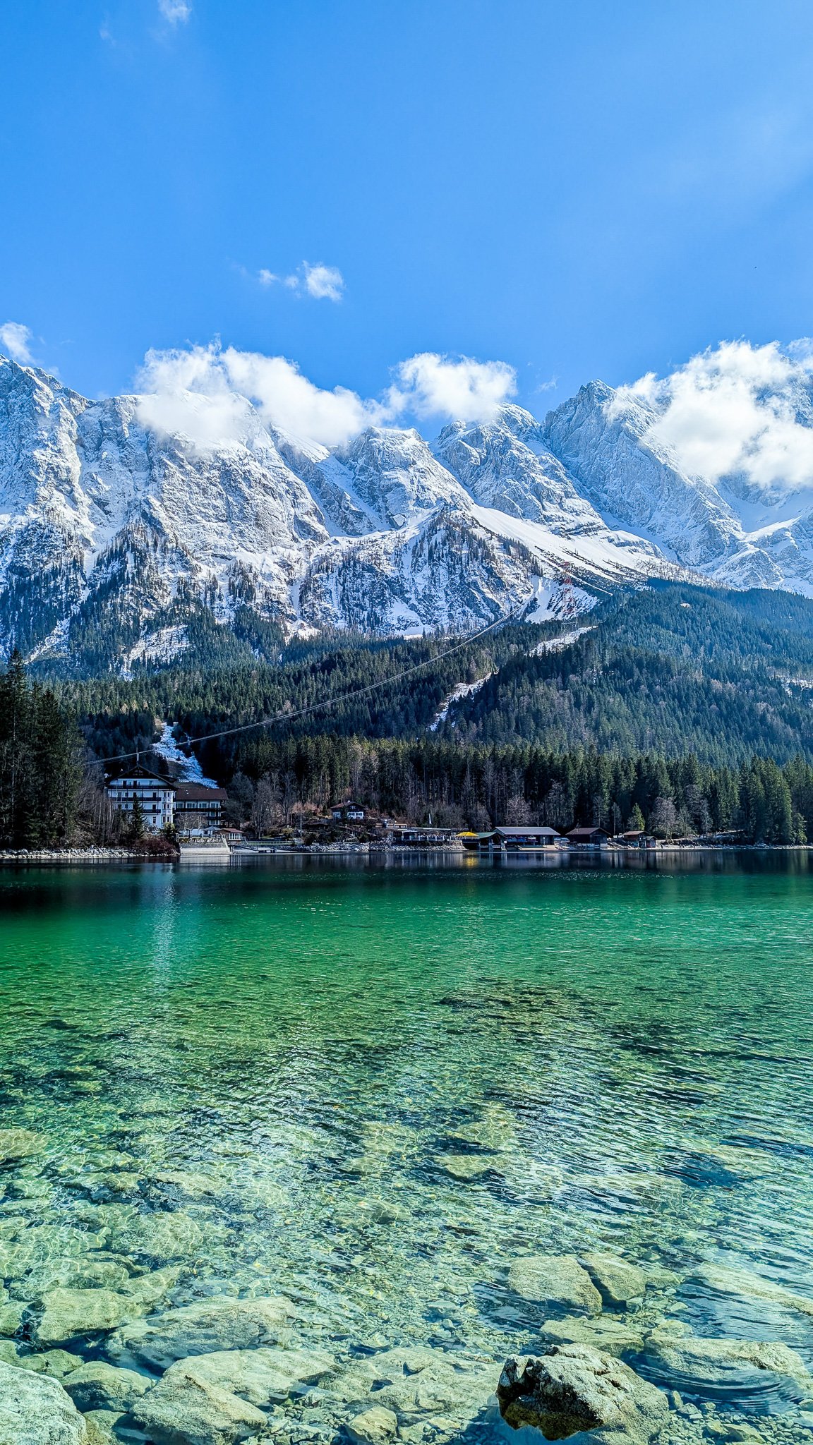 A resort across Lake Eibsee with the Bavarian Alps in the background on a sunny day. The water is very clear.