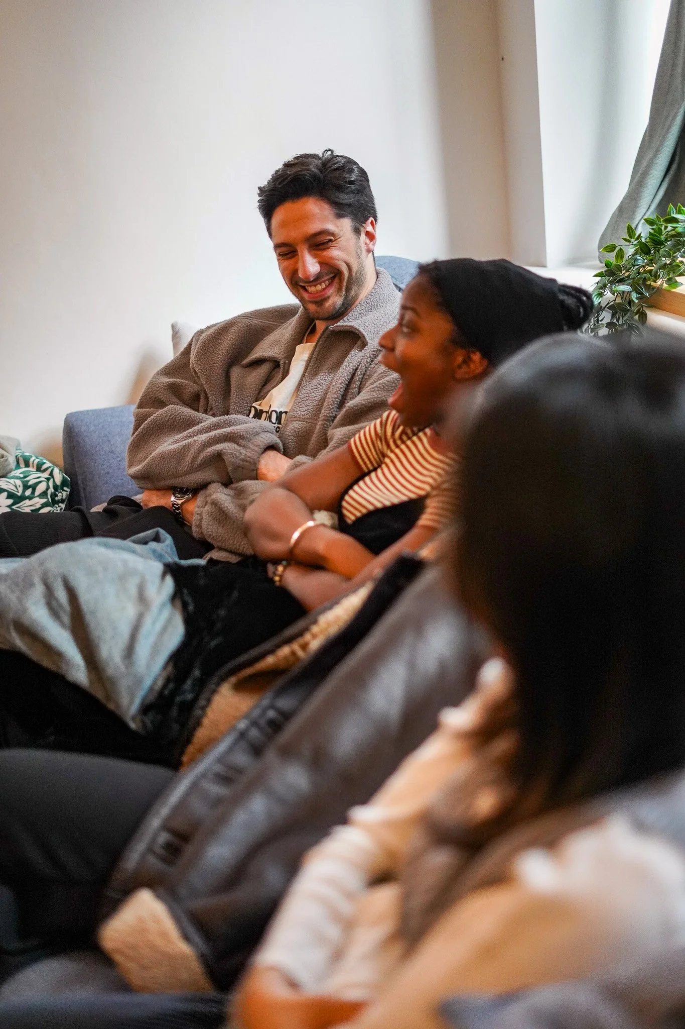 Hispanic man and black woman sitting on a couch at a house party laughing, smiling, and having a good time with friends