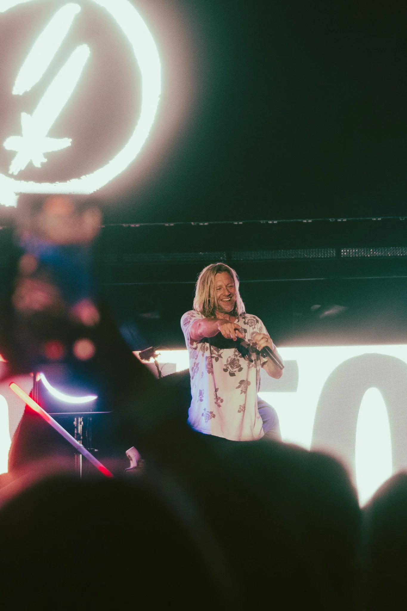 Jon Foreman of Switchfoot singing into a microphone on a stage, pointing to the crowd and smiling at a concert.