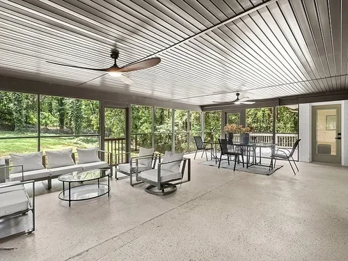 Spacious screened-in porch with outdoor seating, a dining table, and ceiling fans, overlooking a green backyard.
