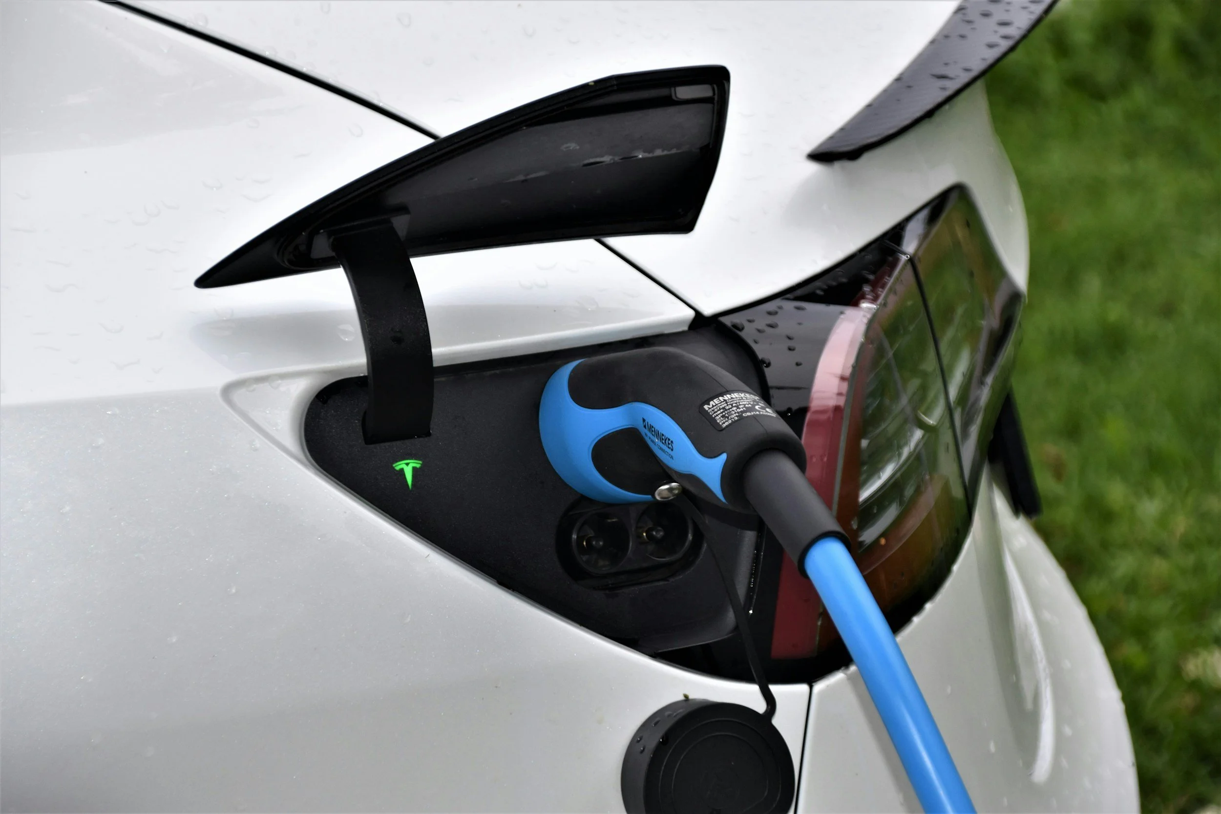 Electric car being charged at a charging station with a visible charging cable plugged into the vehicle.