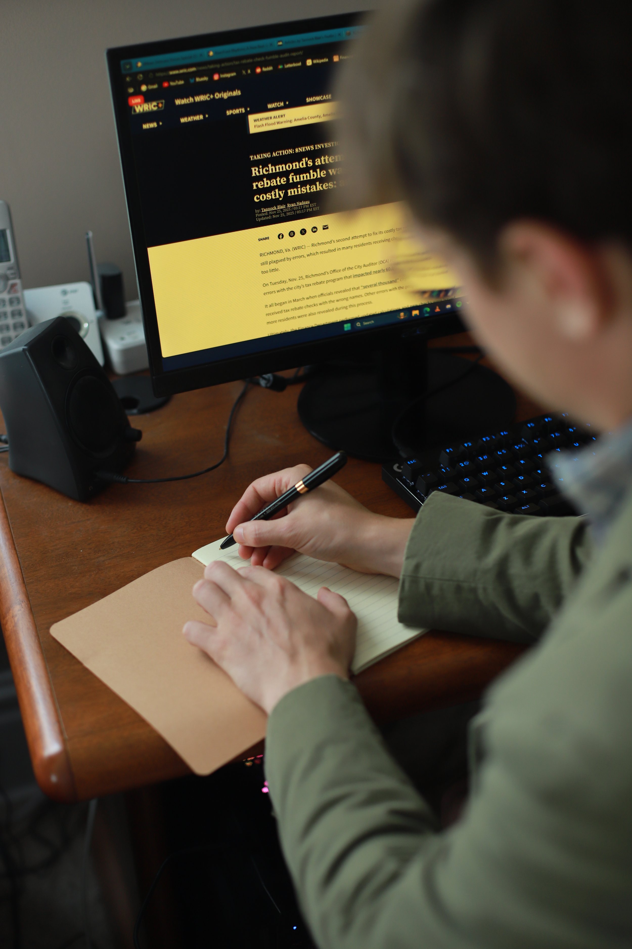 Tannock Blair (Digital Journalist) taking notes while working at a desk with computer monitor displaying a news website.