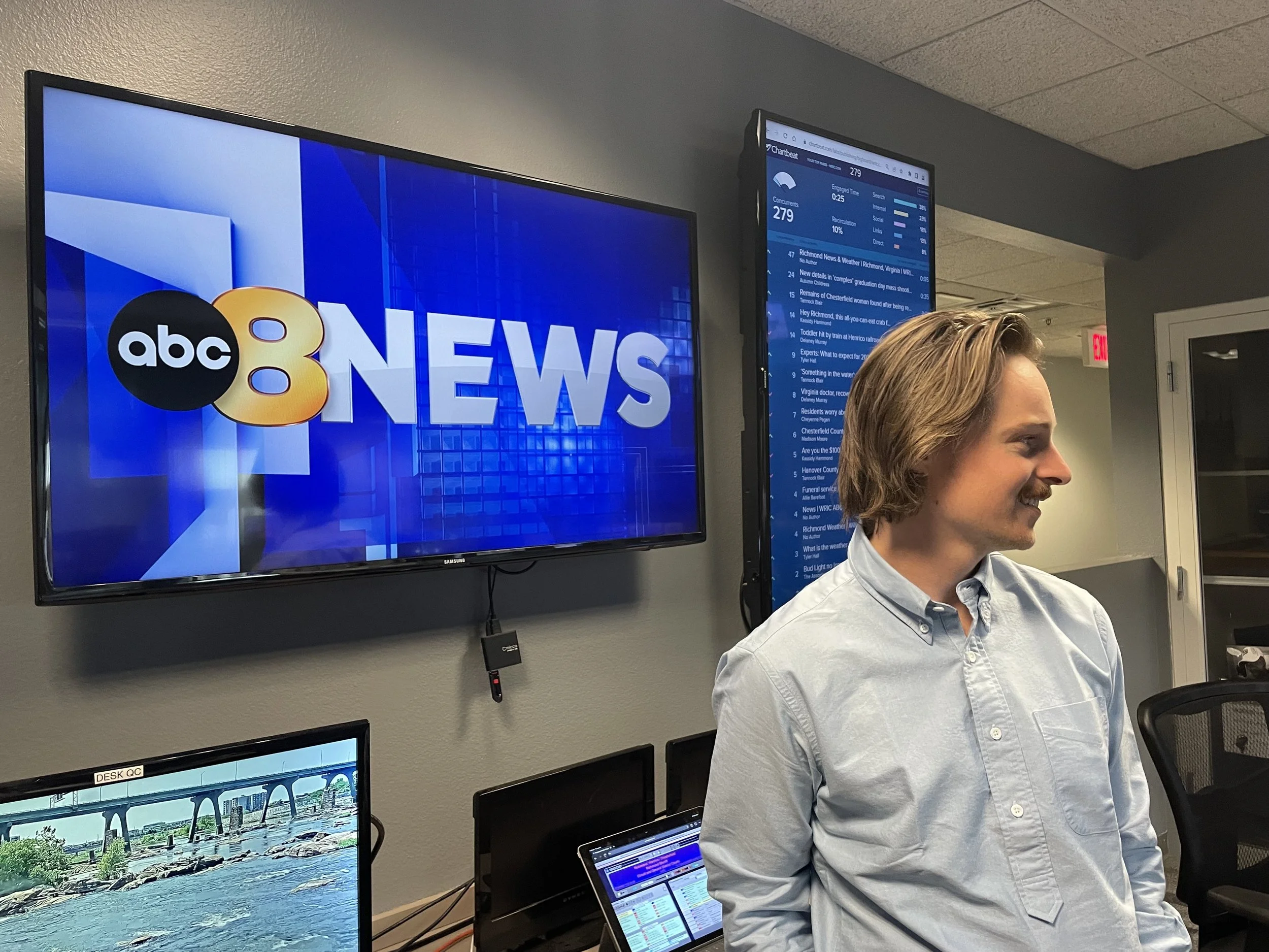 Television screen displaying ABC 8News logo and Tannock Blair (Digital Executive Producer) in an indoor newsroom with multiple monitors and a web browser open.