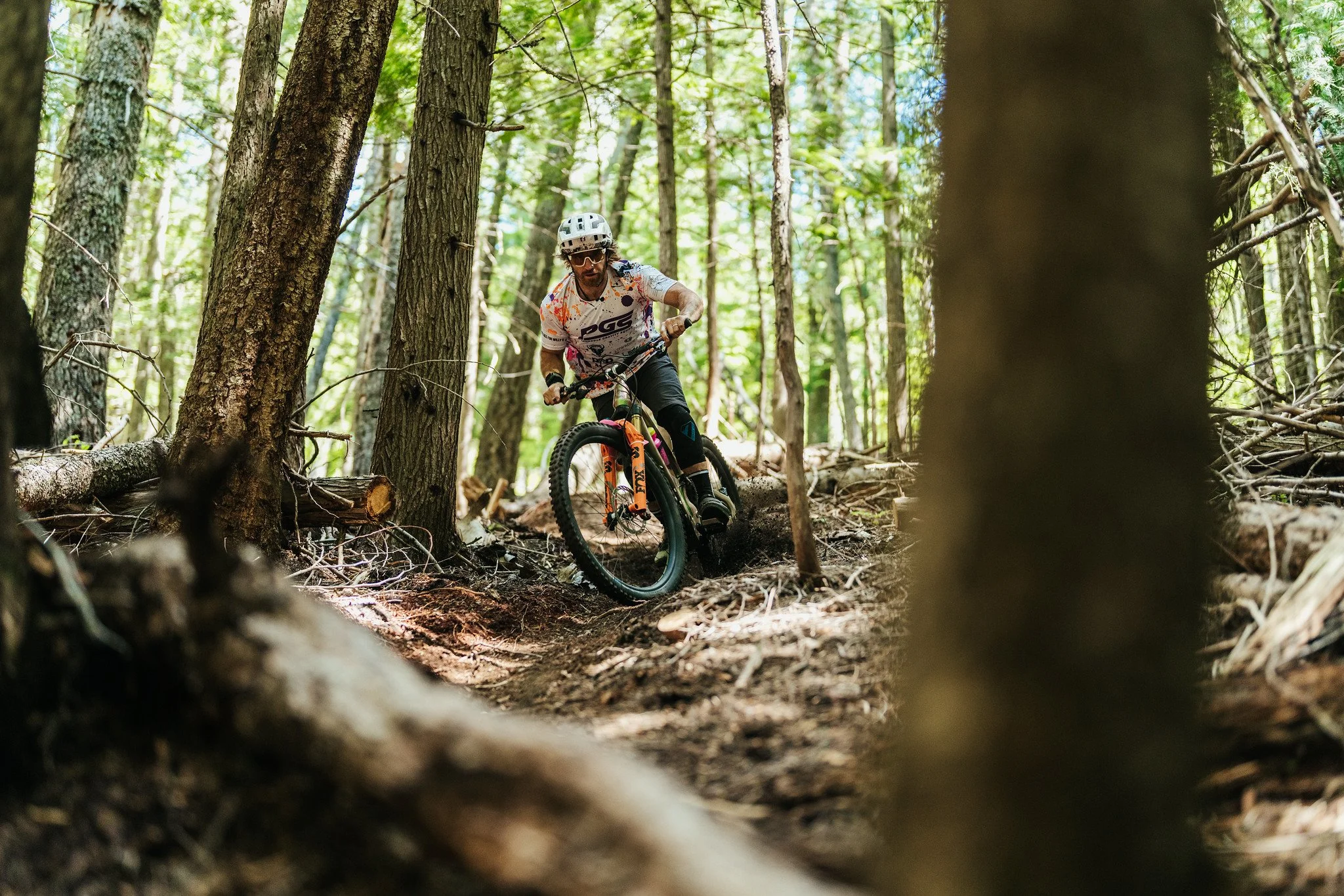 A man mountain biking through a forest trail, surrounded by tall trees and green foliage.