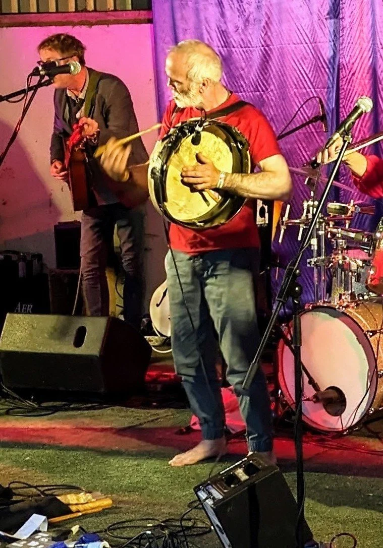 A man playing a bodran with a drumstick and a guitar player in the background during a live performance on stage. Great Irish music scene. Live music in a lot of pubs.