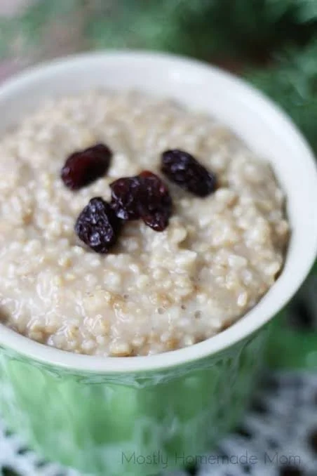 Close-up of a green mug filled with oatmeal topped with dried cranberries. Porridge with honey and berries.