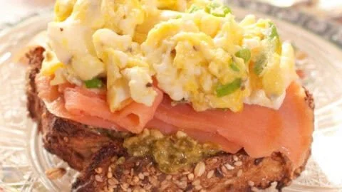 Open-faced sandwich with toasted bread, smoked salmon, scrambled eggs with green onions.