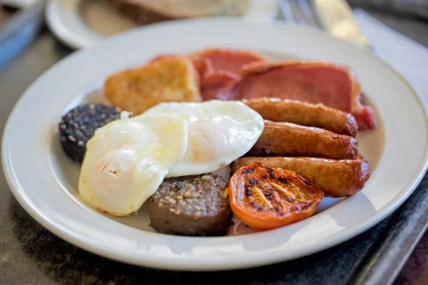 Irish Breakfast plate with eggs, sausage, bacon, grilled tomato, toast, and hash browns. Clonakilty black pudding, sausages, rashers and egg.