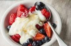A bowl of yogurt topped with fresh strawberries and blueberries, with a spoon on the side.