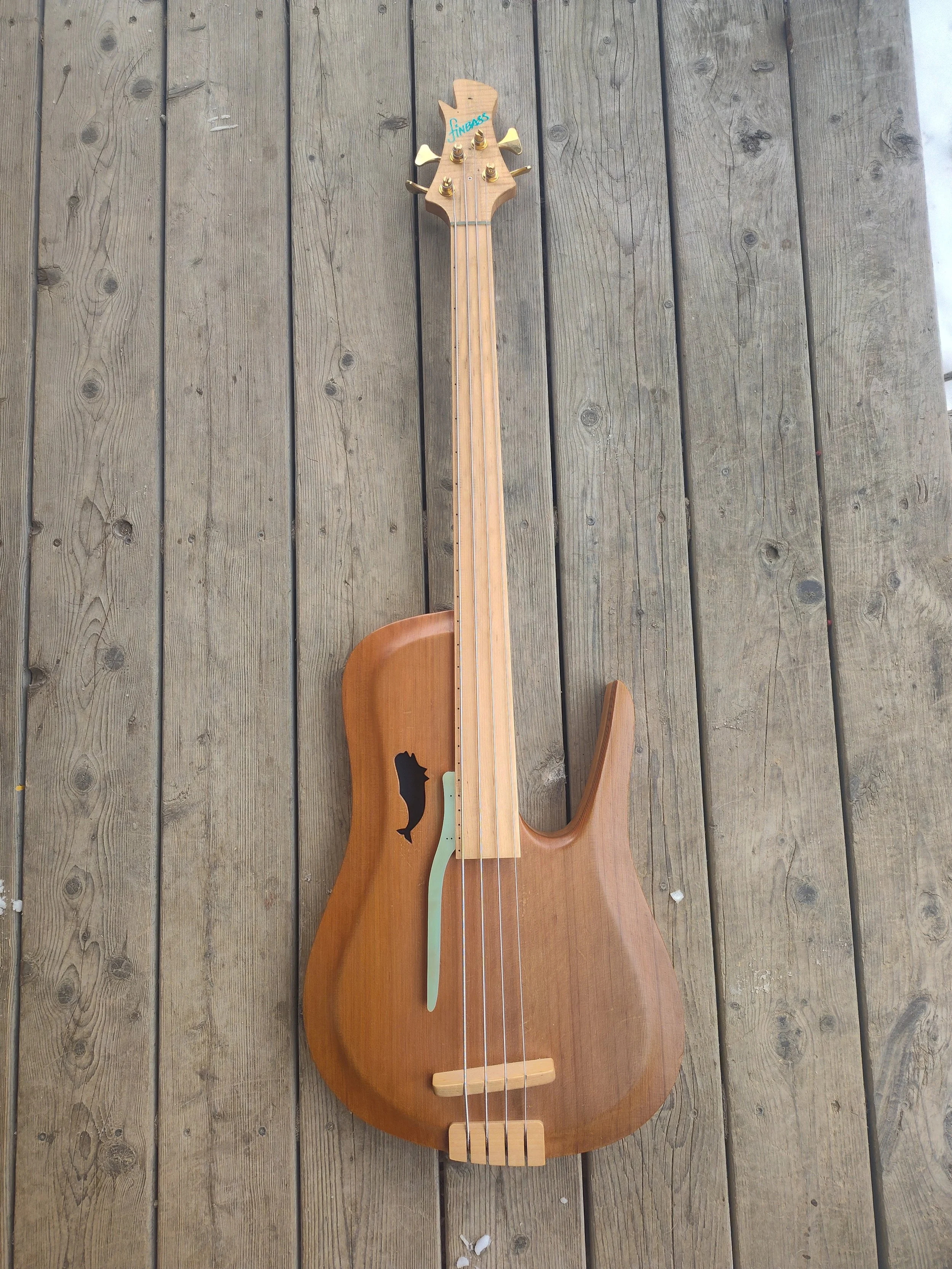 Wooden acoustic bass guitar with a whale silhouette on the body, lying on a wooden deck.