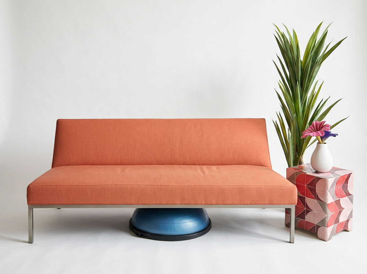 Pink sofa with metal legs next to a tall green plant and a geometric pink patterned side table with a vase of colorful flowers.