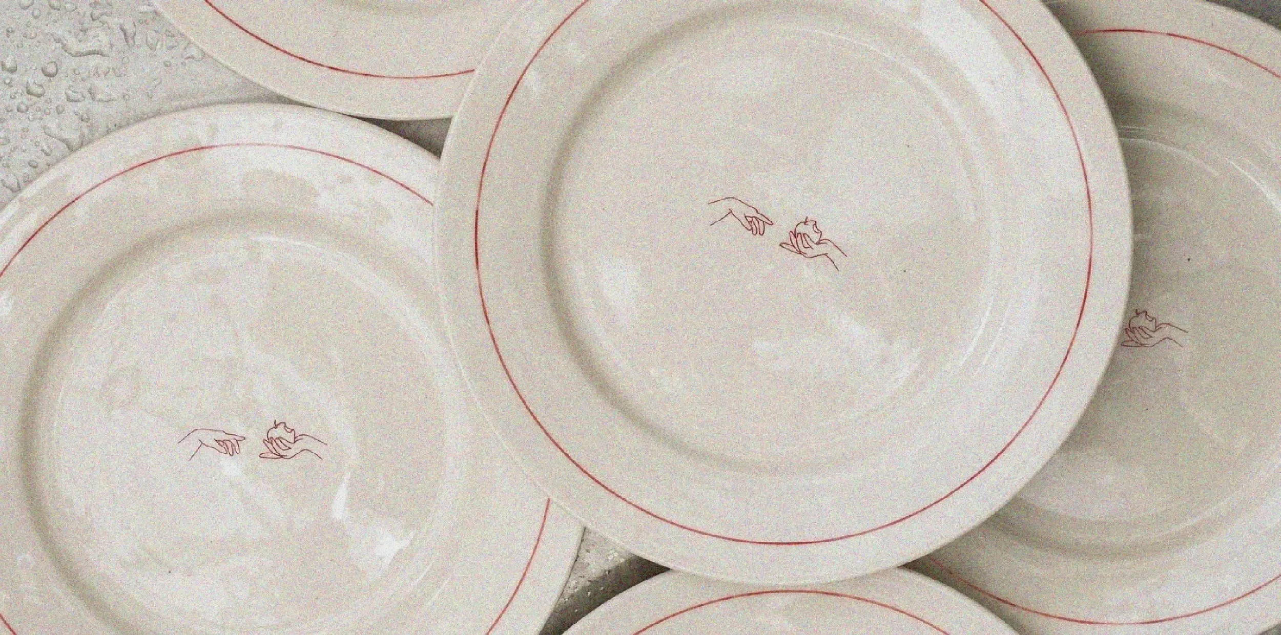 White ceramic plates featuring a simple design of two hands touching, stacked on top of one another.