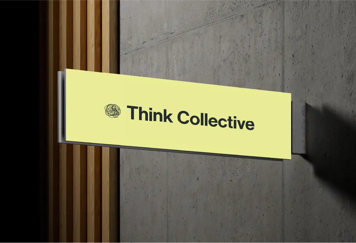 Cartel con fondo amarillo y texto en negrita que dice "Think Collective", ubicado en una pared de concreto con detalles de madera.