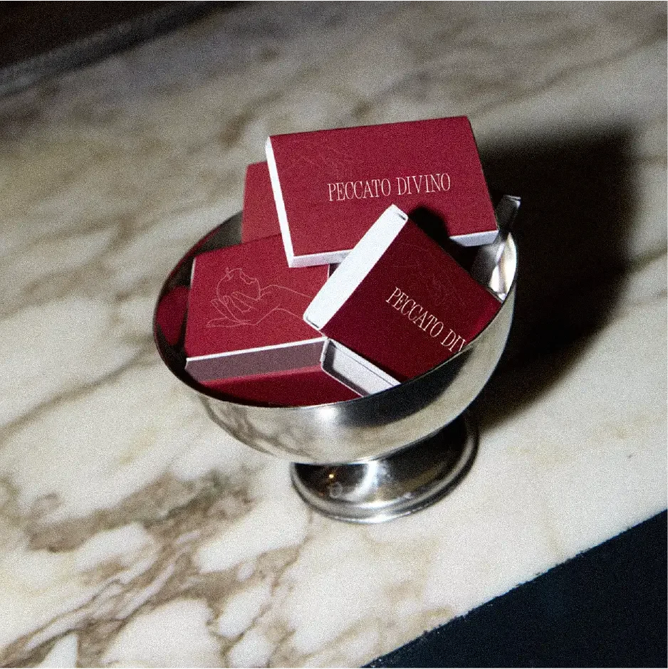 Red boxes with white lettering that reads “Pecatto Divino” inside a metal container on a marble table.