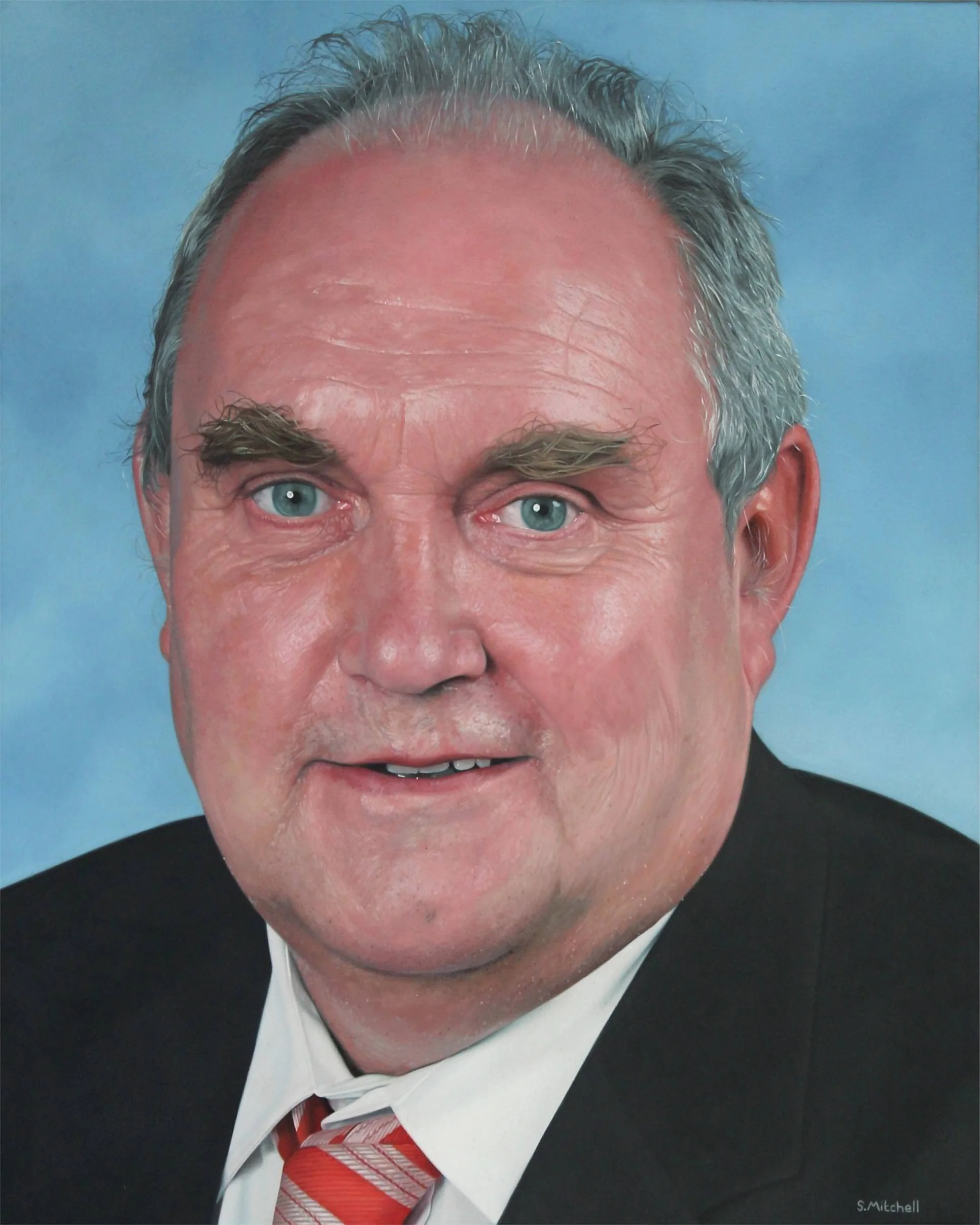 Close-up portrait of an elderly man with gray hair, blue eyes, wearing a black suit, white shirt, and red striped tie, against a blue background.