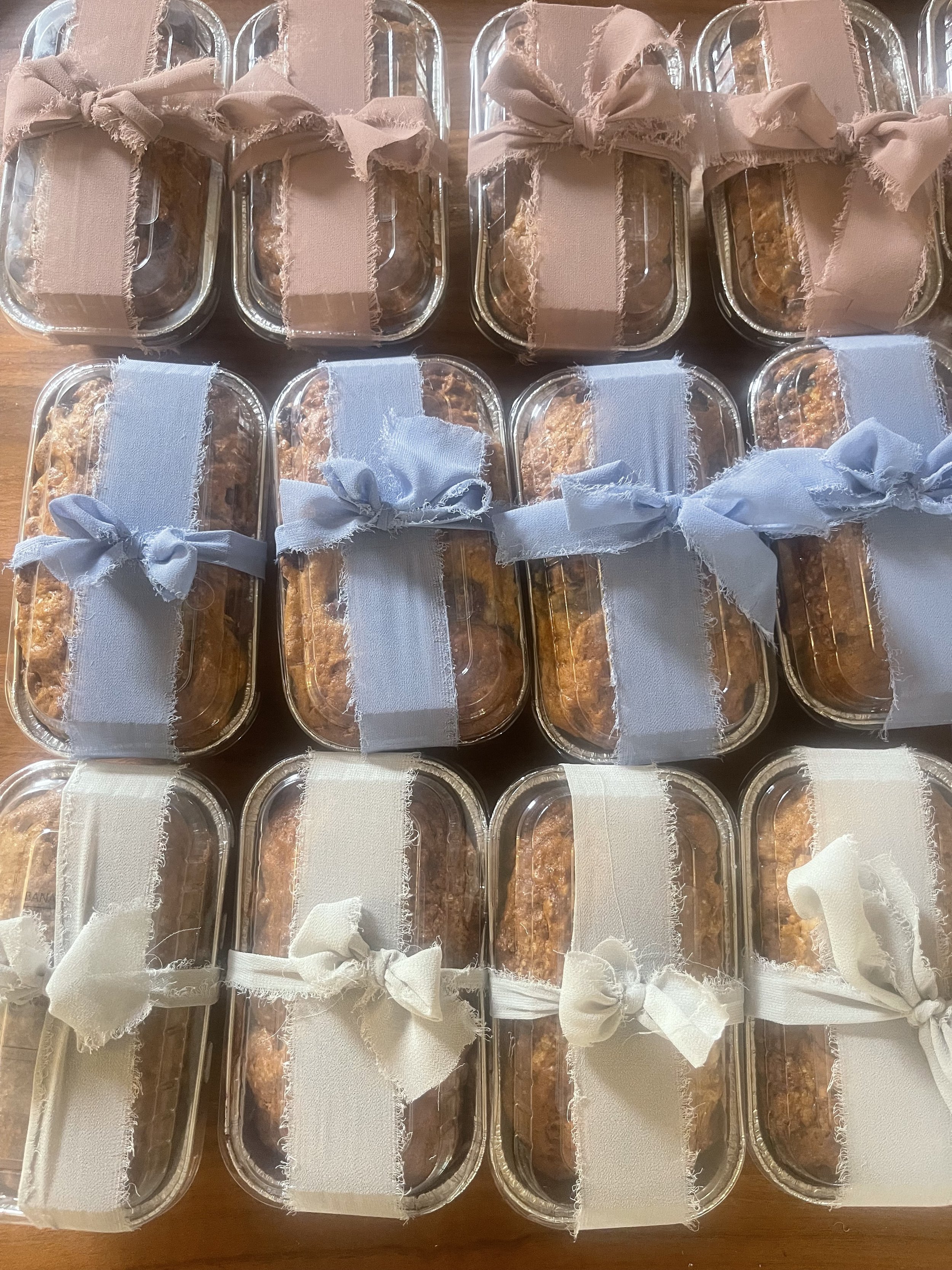 Several small glass food containers filled with baked goods, each tied with a cloth ribbon in various pastel colors including beige, light blue, and white.