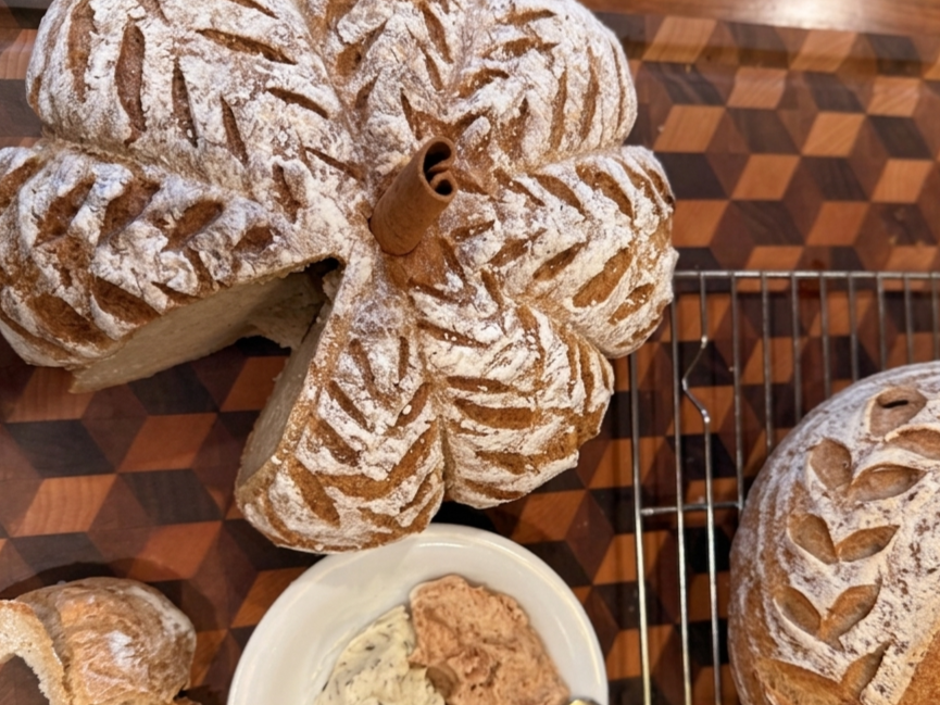 A beautifully baked bread with a flower shape, dusted with powdered sugar, and a small cinnamon stick on top. The bread has a leaf pattern on its surface.