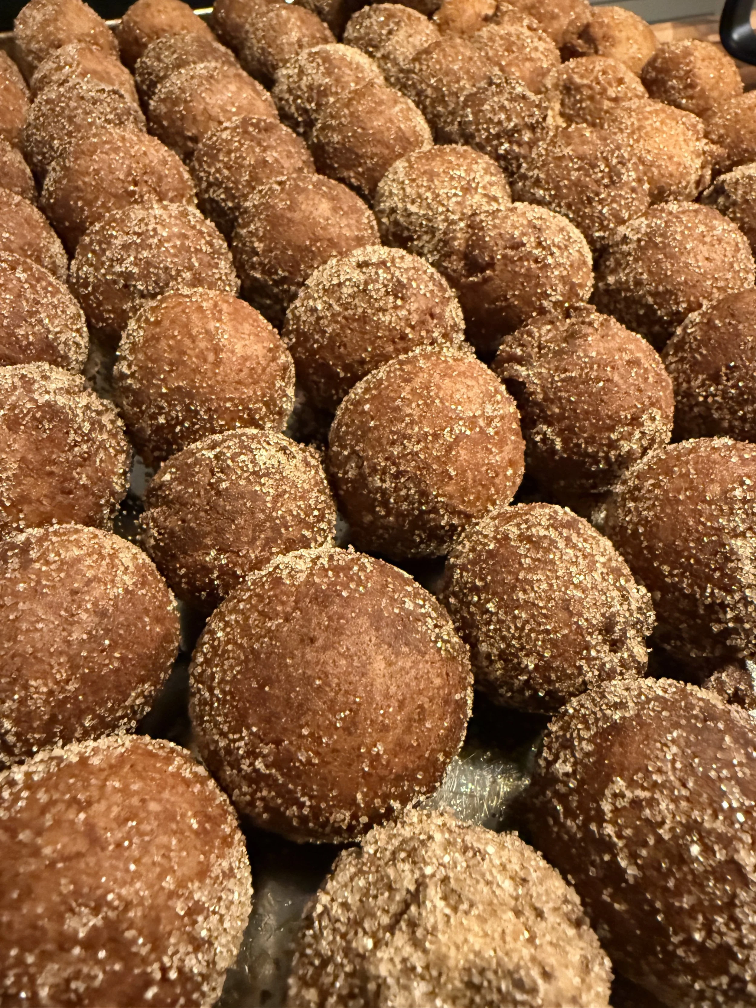 Close-up of numerous sweet truffles covered in cocoa powder and sugar, arranged on a tray.