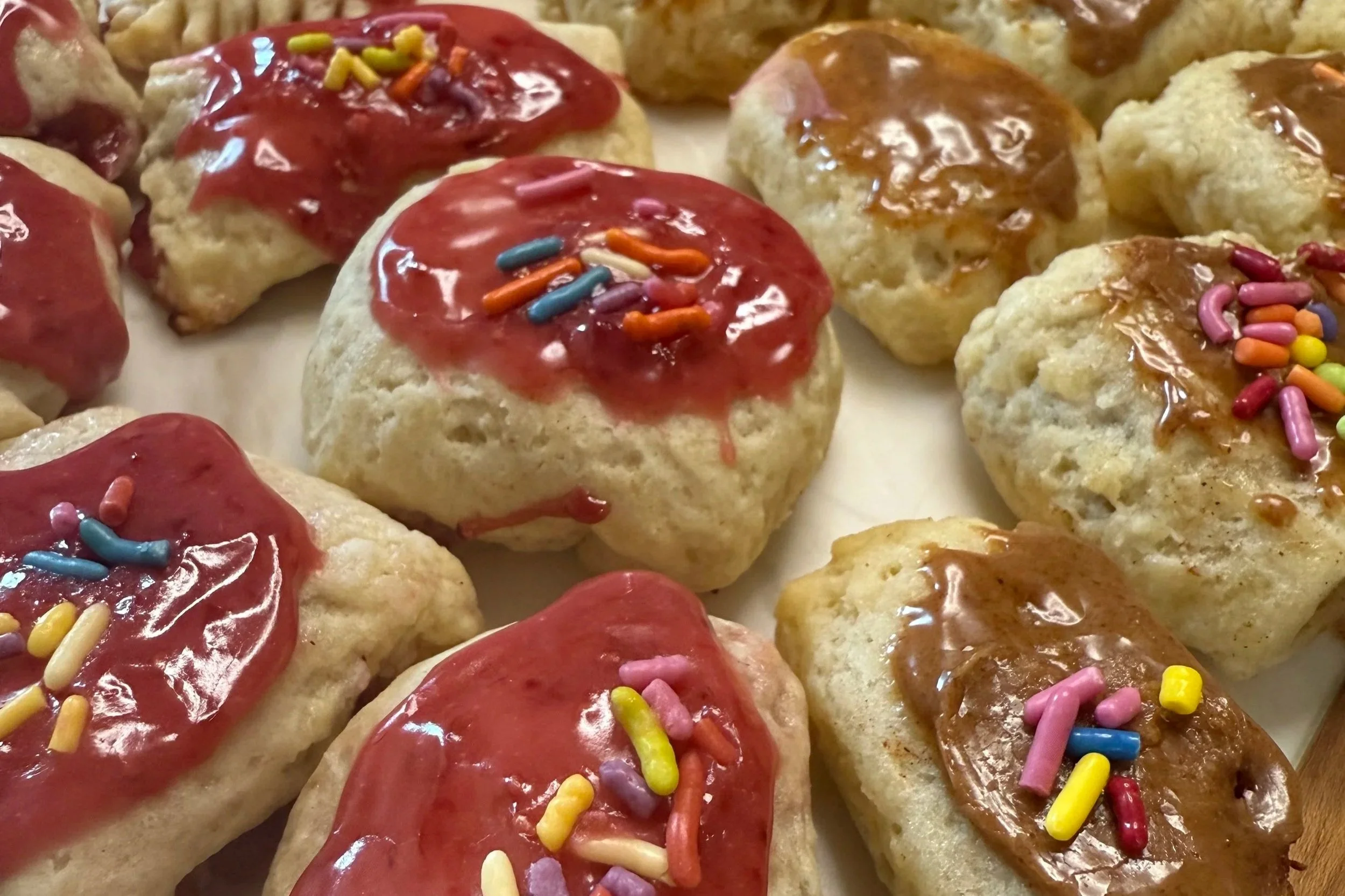 Assorted cookies with red icing and colorful sprinkles, with some cookies having caramel or chocolate drizzles.