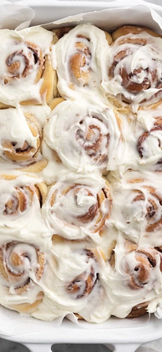 A tray of freshly baked cinnamon rolls topped with creamy white icing.