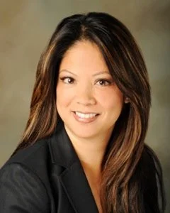 Professional woman with long dark brown hair, wearing a black blazer and smiling at the camera.