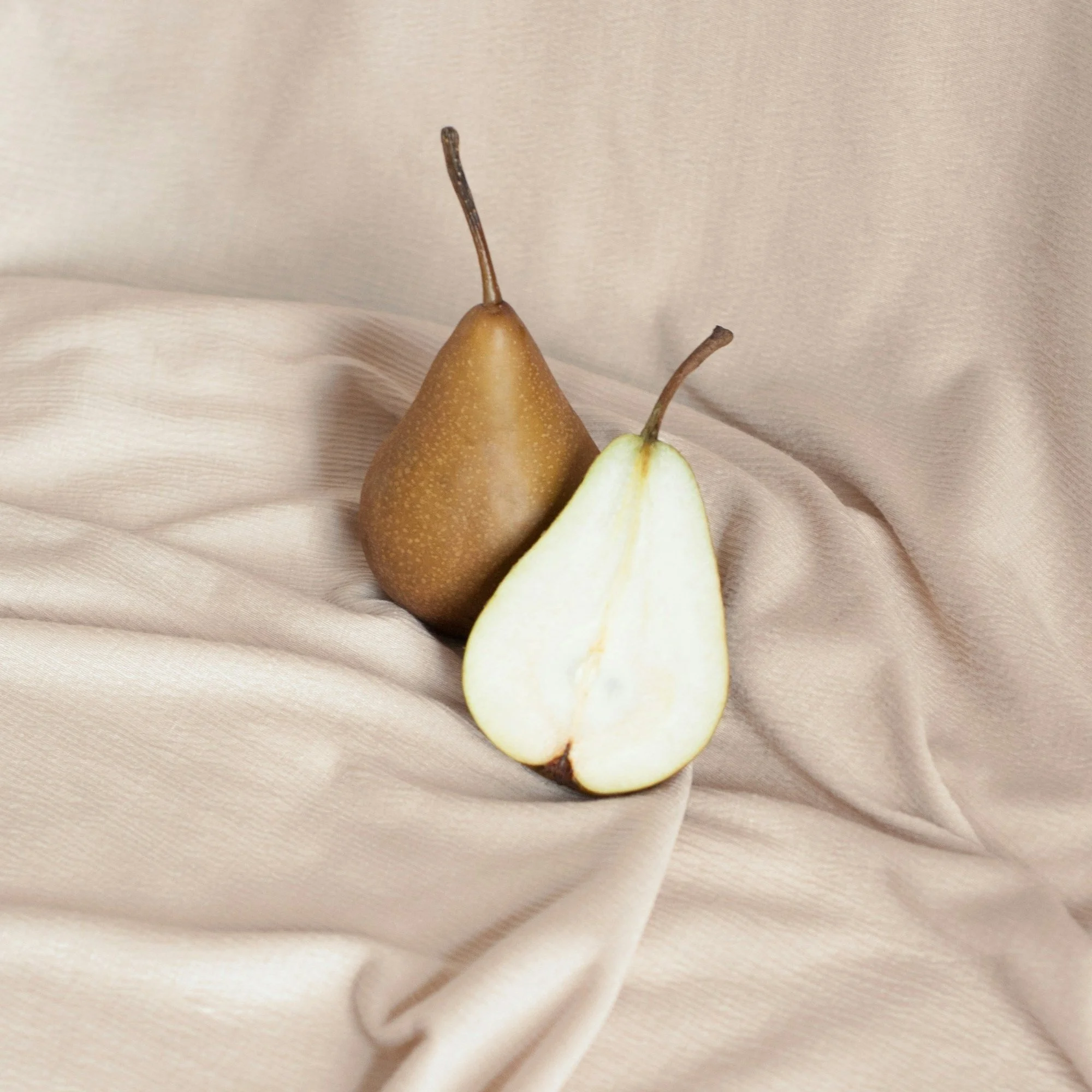 A whole pear and a sliced pear half on a beige fabric surface.