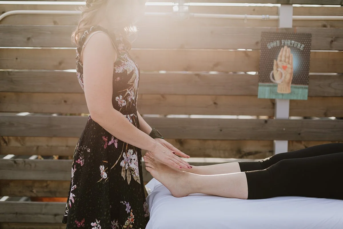 A woman giving a foot massage to another person lying on a table outdoors