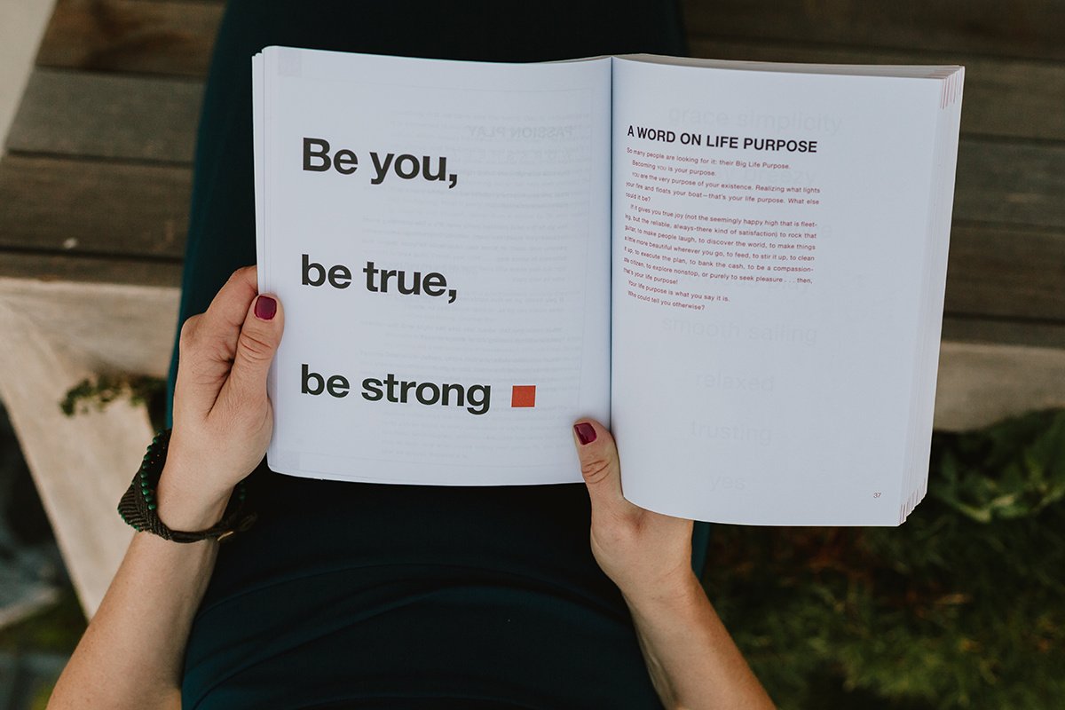 Person holding open book with the text 'Be you, be true, be strong' in large font.