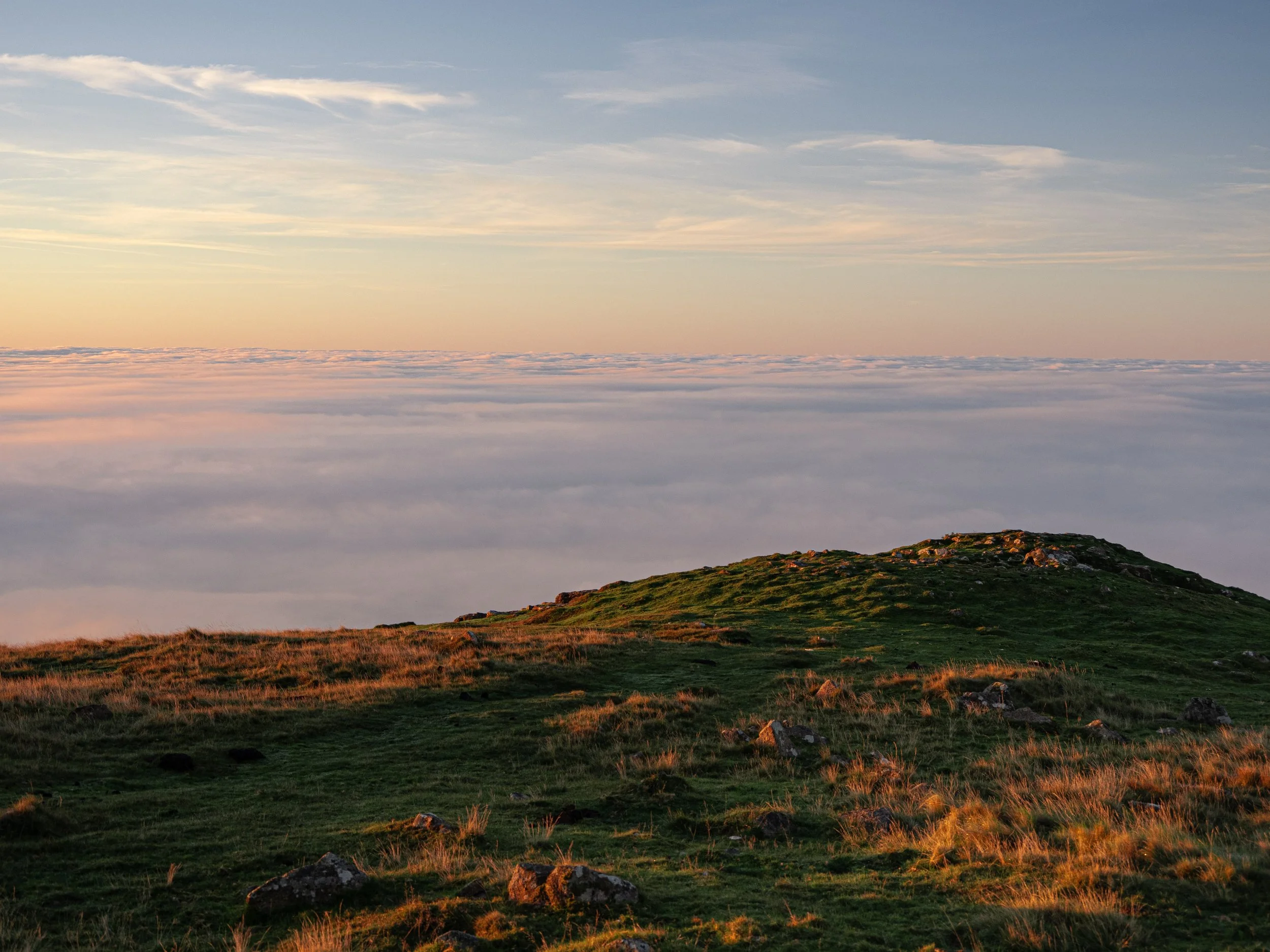 Sunset over a rocky grassy hilltop above a sea of clouds