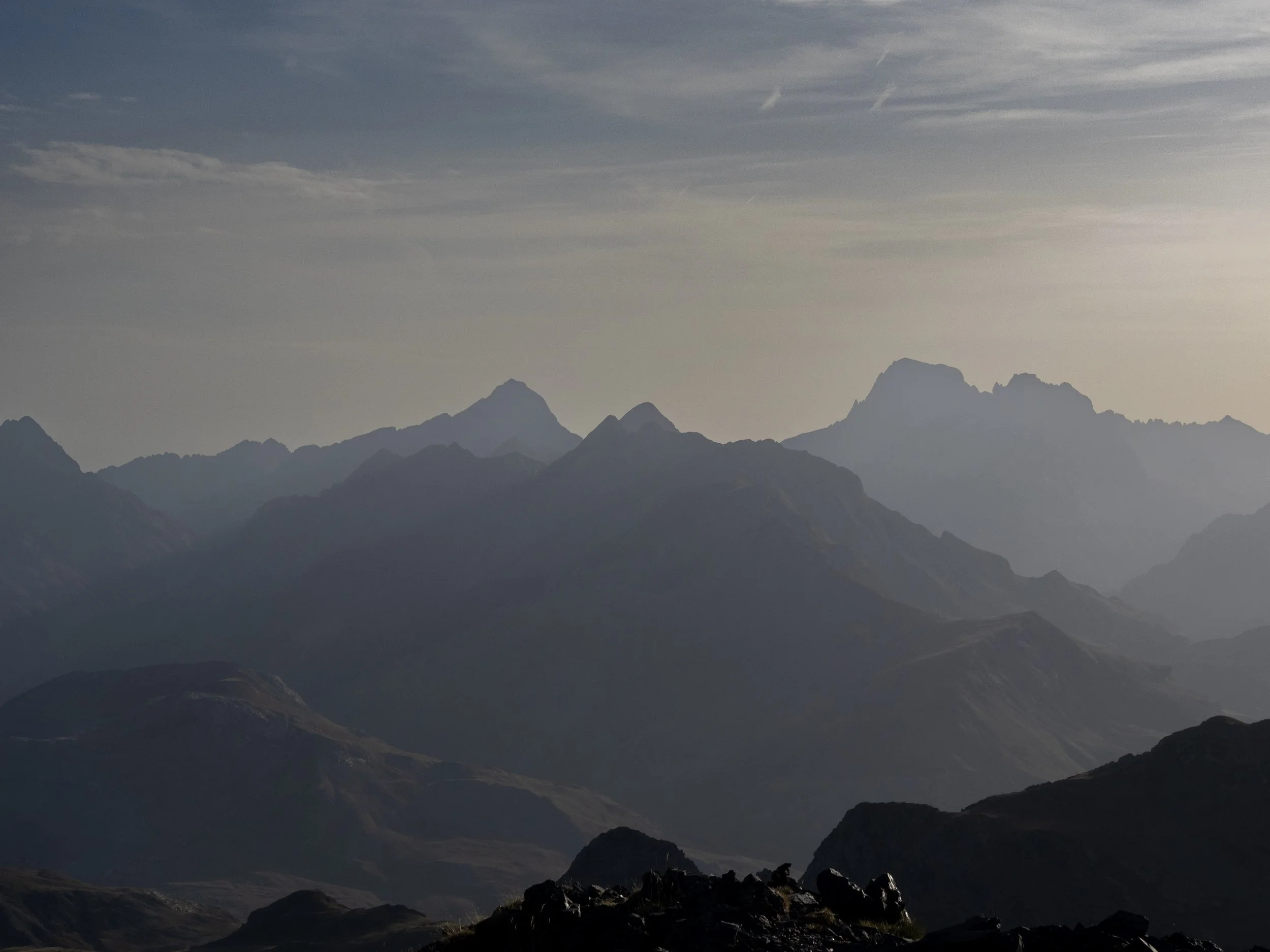 Misty layered mountain range silhouetted beneath a cloudy sky at dusk
