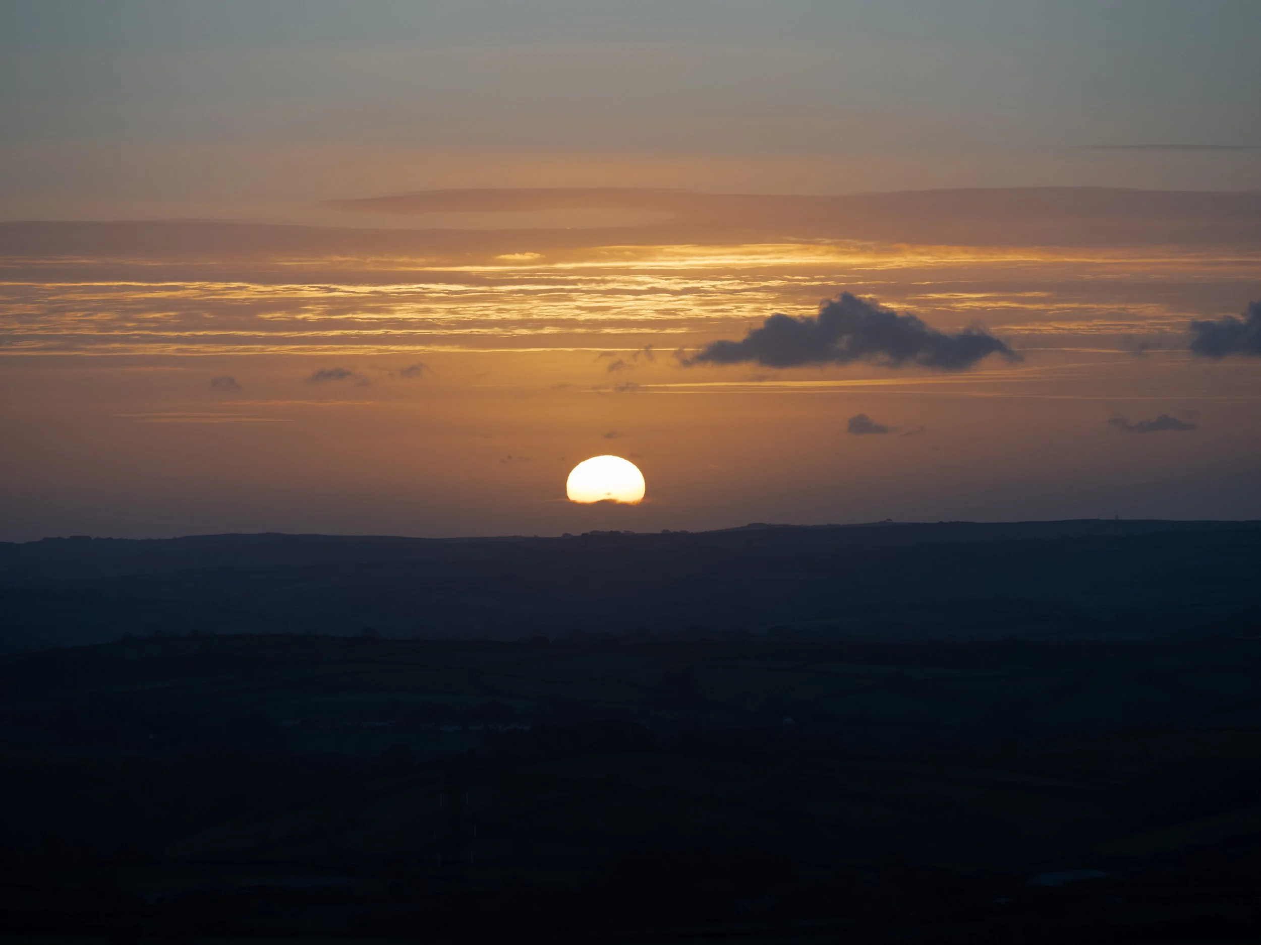 Sunset over a dark silhouetted horizon with glowing orange clouds