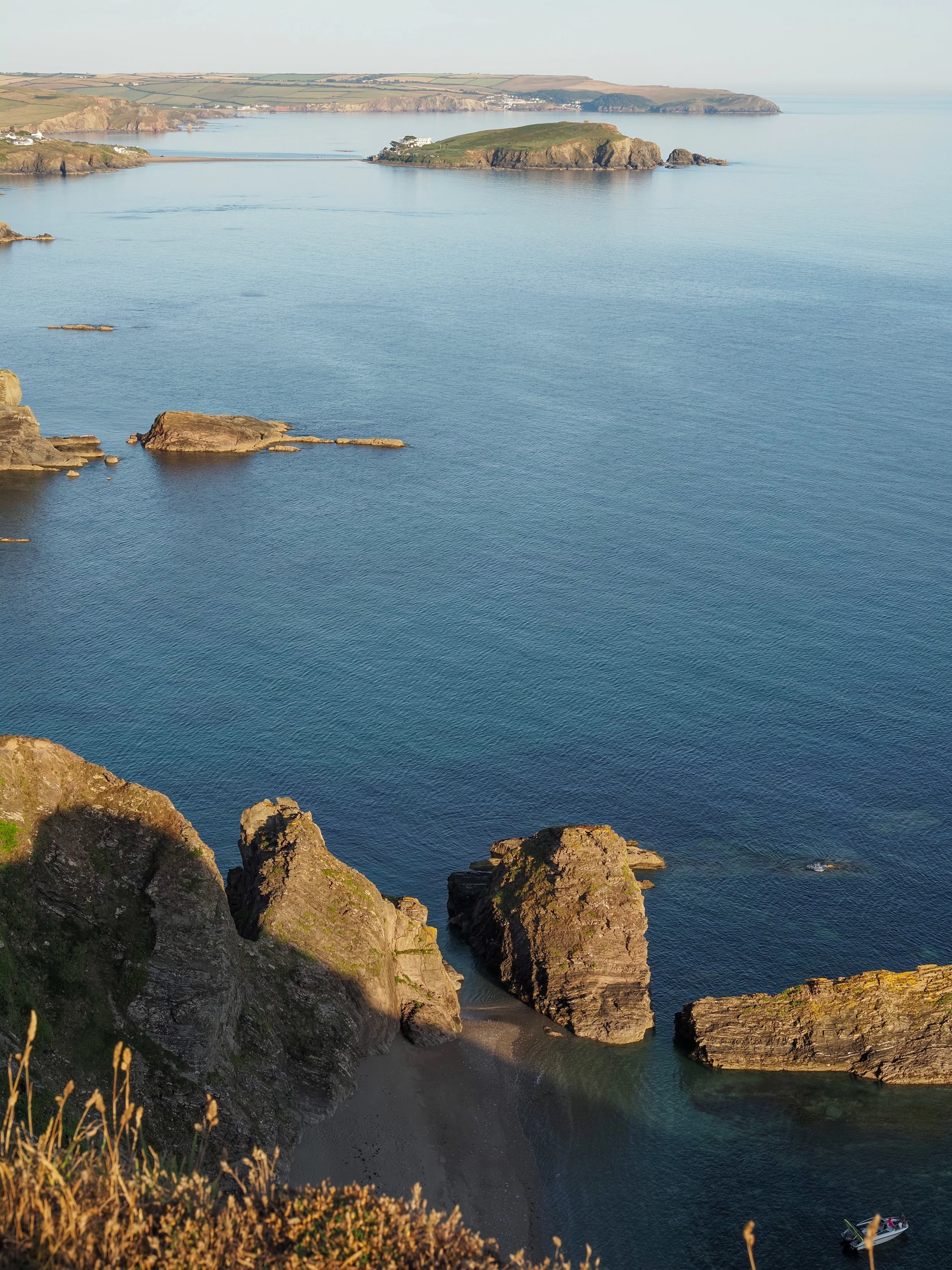 Panoramic coastal view of rugged cliffs, sea stacks, a small beach, and a green peninsula with seaside villages.